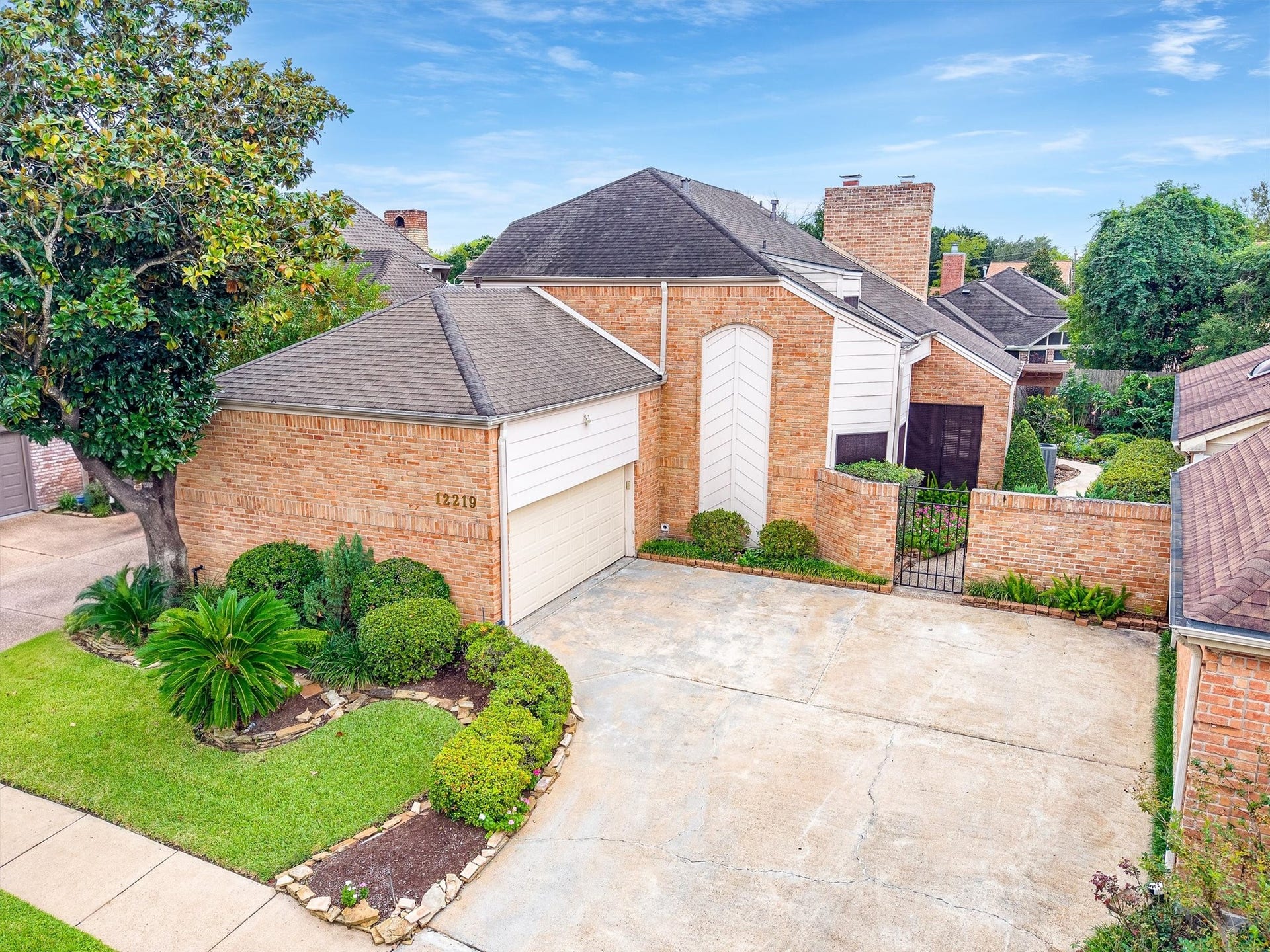 12219 Ravenmoor Drive, Houston, TX 77077 Charming brick home with a two-car garage, lush landscaping, and a gated entrance, offering privacy and curb appeal.