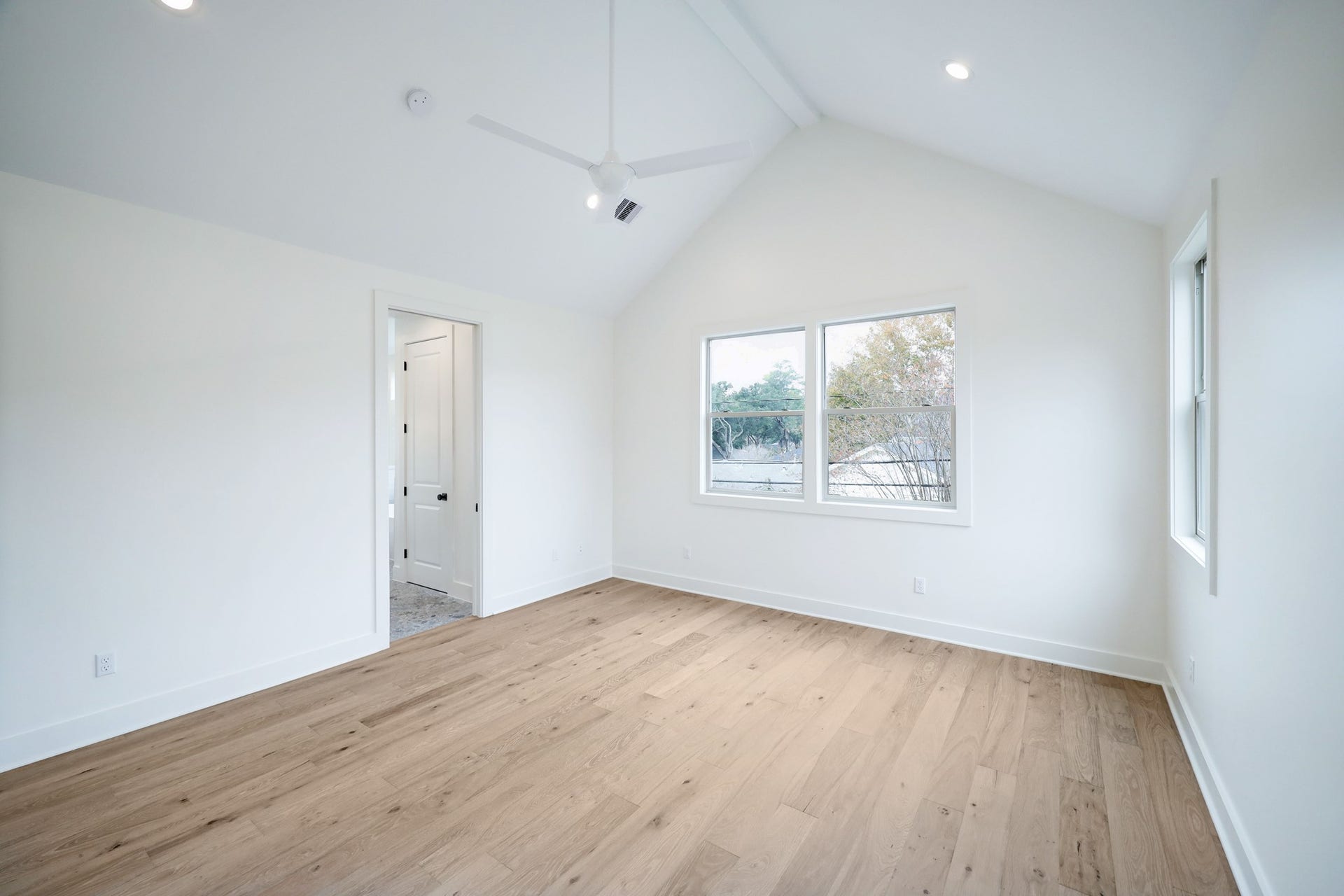 The smooth walls, neutral color palette and vaulted ceiling accentuate the open space found in the primary bedroom. Recessed lighting and large windows illuminate the space. *Previous Project*