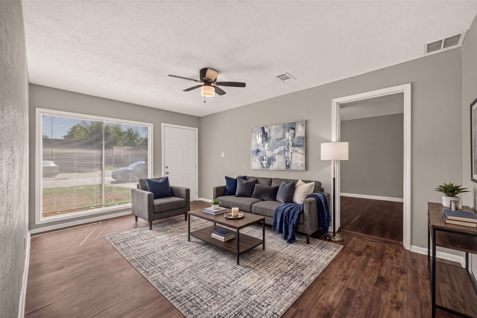 5935 Beldart Street, Houston, TX 77033 Living room with large front window and ceiling fan, open to the hallway. (Virtually staged)
