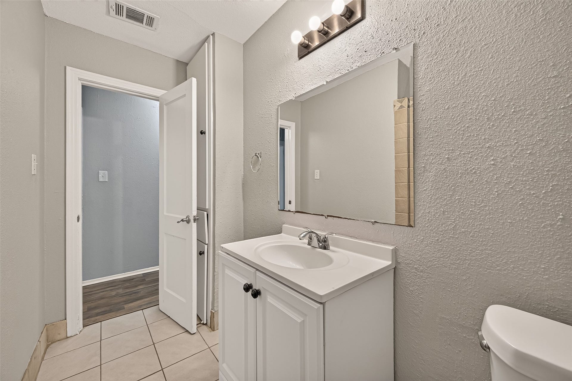 5935 Beldart Street, Houston, TX 77033 Hall bath with white vanity, tile flooring, and vanity lighting.