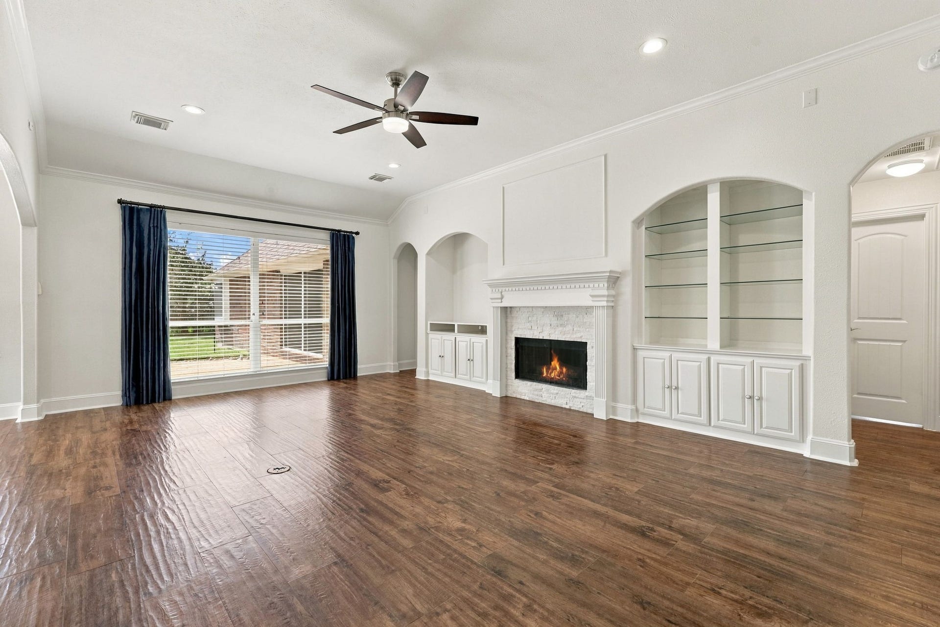 33211 Woodton Court, Fulshear, TX 77441 The Family Room is gorgeous and inviting, featuring 10-foot ceilings, elegant crown molding, 5-inch baseboards, and beautiful wood-look tile flooring. Expansive windows with custom drapes fill the room with natural light, while a gas-log fireplace surrounded by stacked stone creates a warm focal point. Convenient built-ins on either side of the fireplace provide the perfect combination of style and functionality.