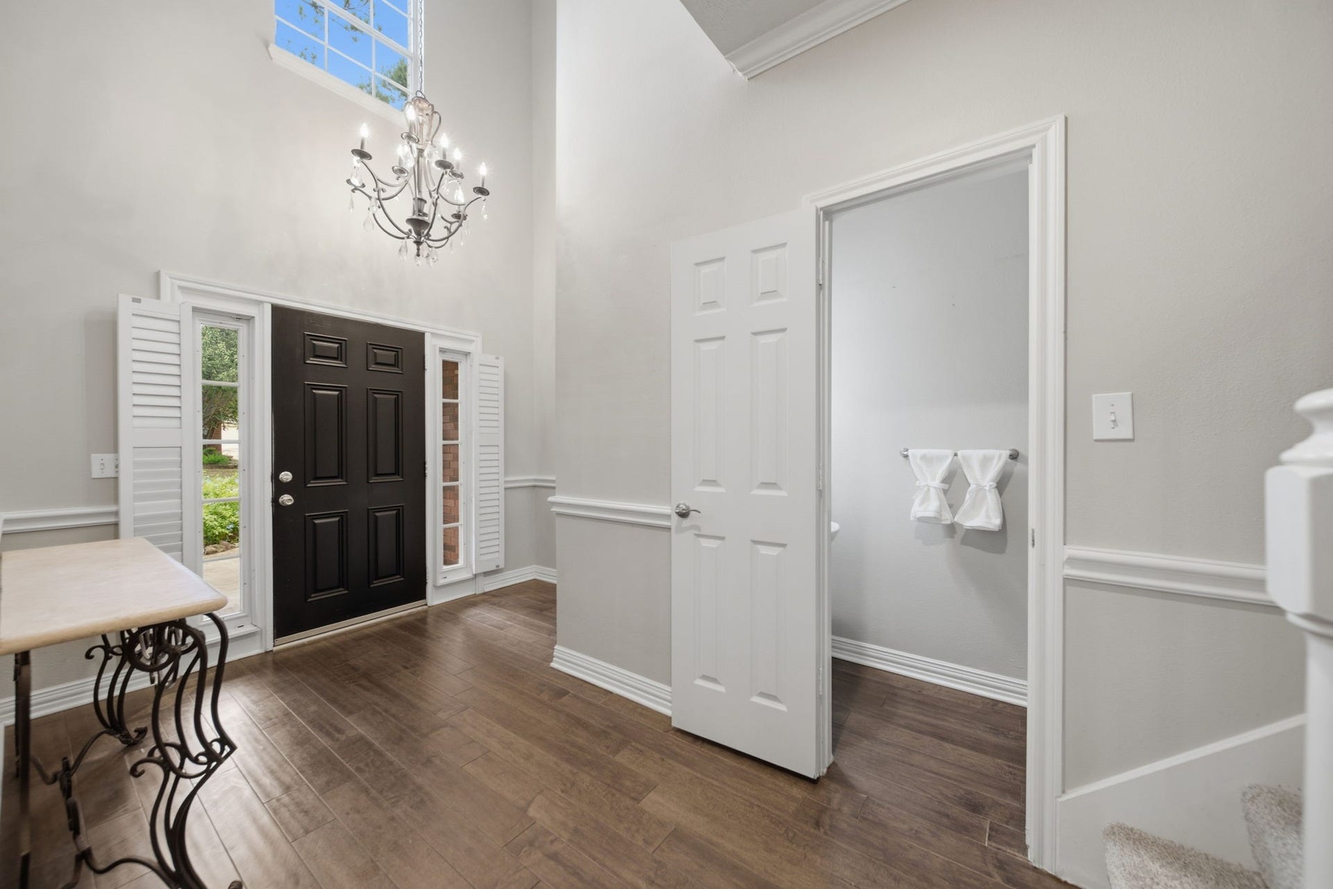 99 E Sterling Pond Circle, The Woodlands, TX 77382 Elegant entryway featuring a grand chandelier, high ceilings, and rich wood flooring, with convenient access to the powder room.