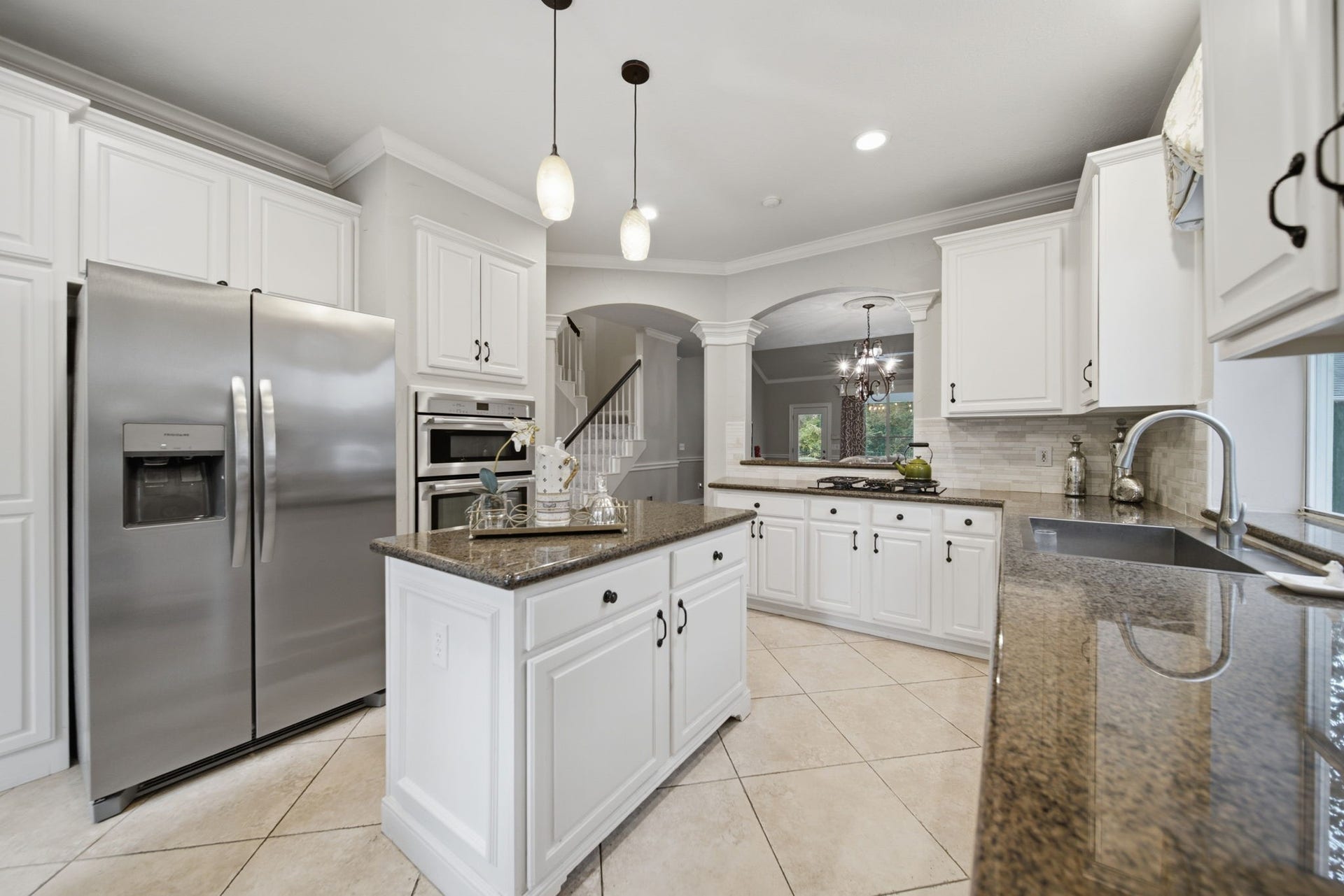 99 E Sterling Pond Circle, The Woodlands, TX 77382 This elegant kitchen featuring white cabinetry, granite countertops, and stainless steel appliances including the refrigerator opens up to the living area. The space is complemented by a central island, stylish pendant lighting, and a spacious layout with ample natural light creating a welcoming setting for everyday living.