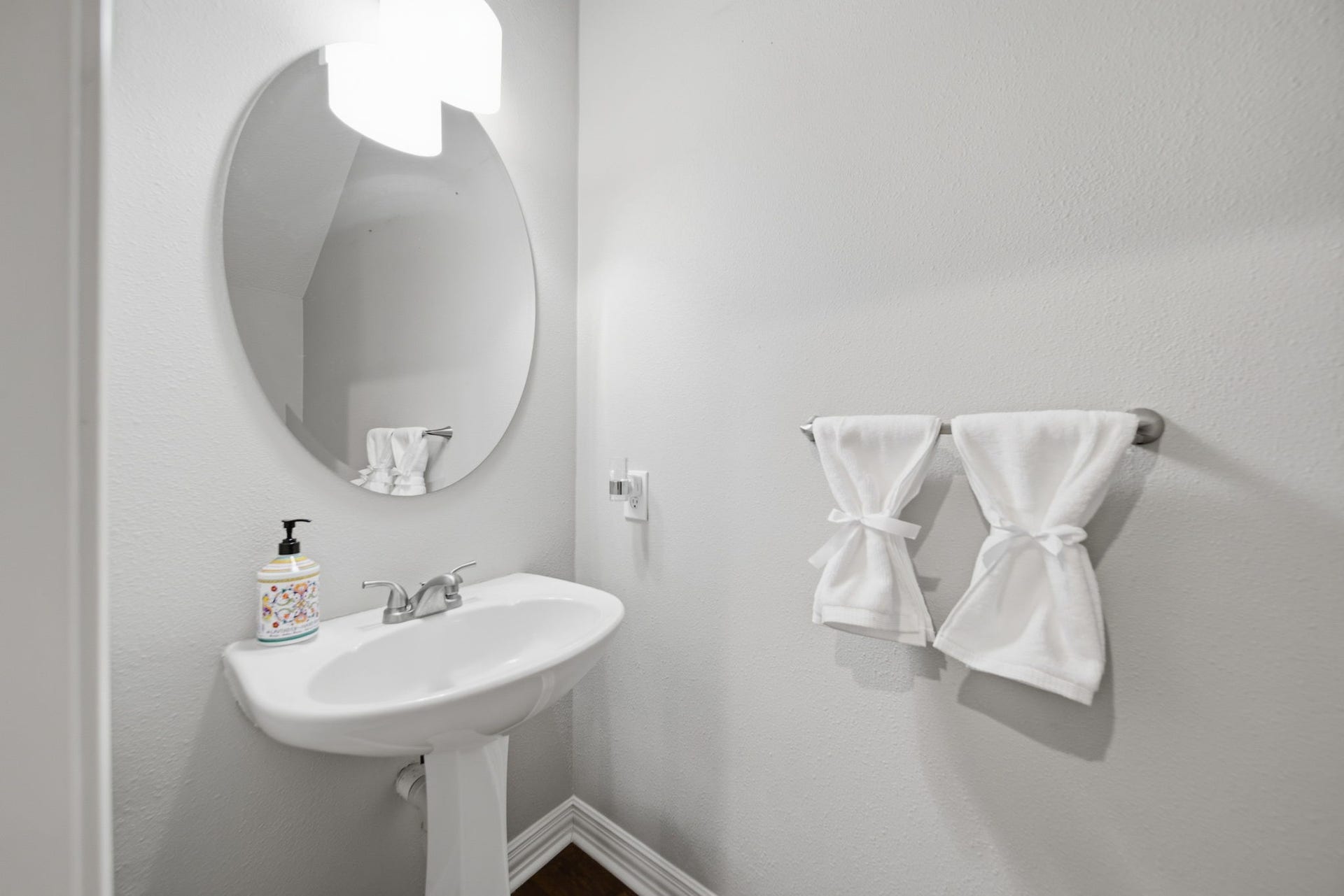 99 E Sterling Pond Circle, The Woodlands, TX 77382 Charming powder room with a sleek pedestal sink, elegant oval mirror, and modern lighting.