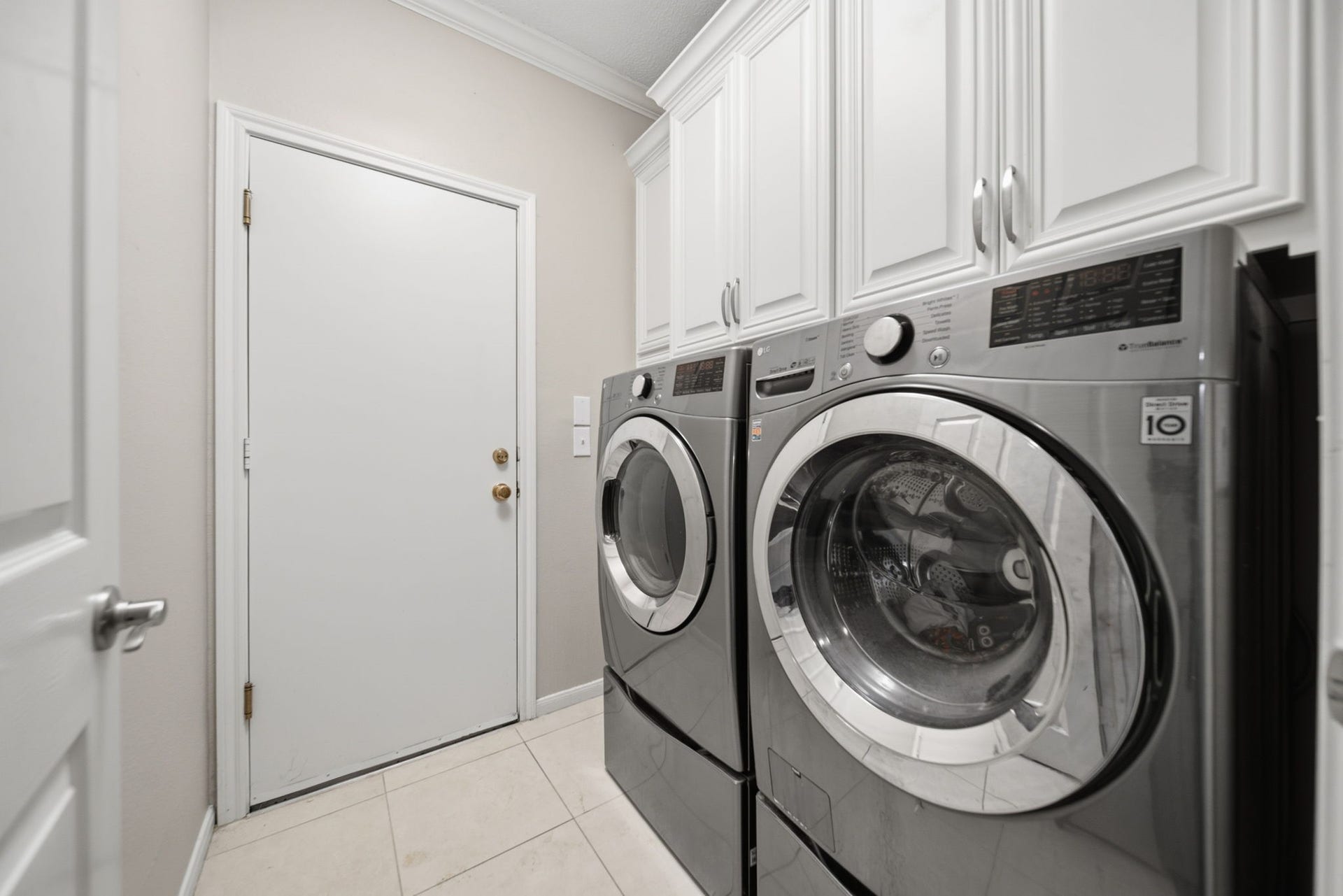 99 E Sterling Pond Circle, The Woodlands, TX 77382 Added cabinetry surrounds the included washer & dryer, providing generous storage and a custom finished look in this well-organized laundry room. An additional storage closet is tucked behind the door in the foreground, offering convenient space for household essentials.