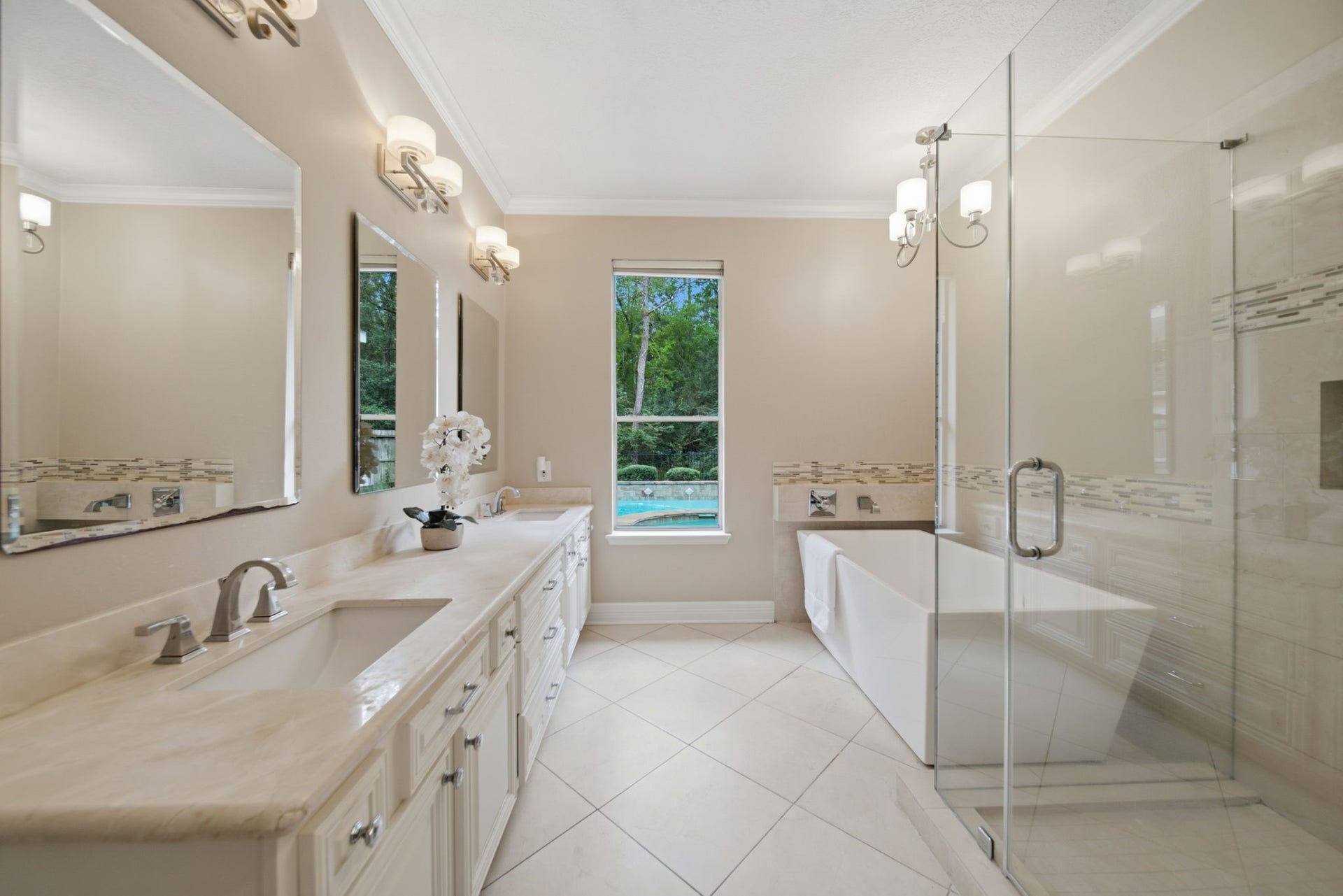 99 E Sterling Pond Circle, The Woodlands, TX 77382 This beautifully updated master bath features a freestanding soaking tub, separate frameless glass shower, and an expansive double-sink vanity with white cabinetry and generous storage. The updated lighting, soft neutral finishes, and natural light create an inviting retreat for you after a long day.