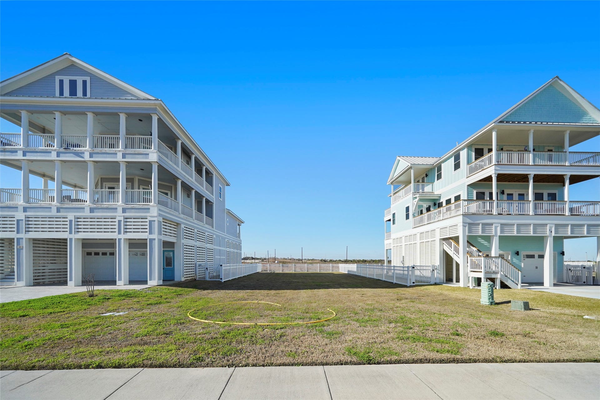 Street-level view from the homesite toward the Gulf demonstrates the property's close relationship to the water and the scale of the neighboring coastal residences. The cleared 50'  120' lot is positioned between two existing homes, providing a valuable real-world reference for the size and potential massing of a future residence.