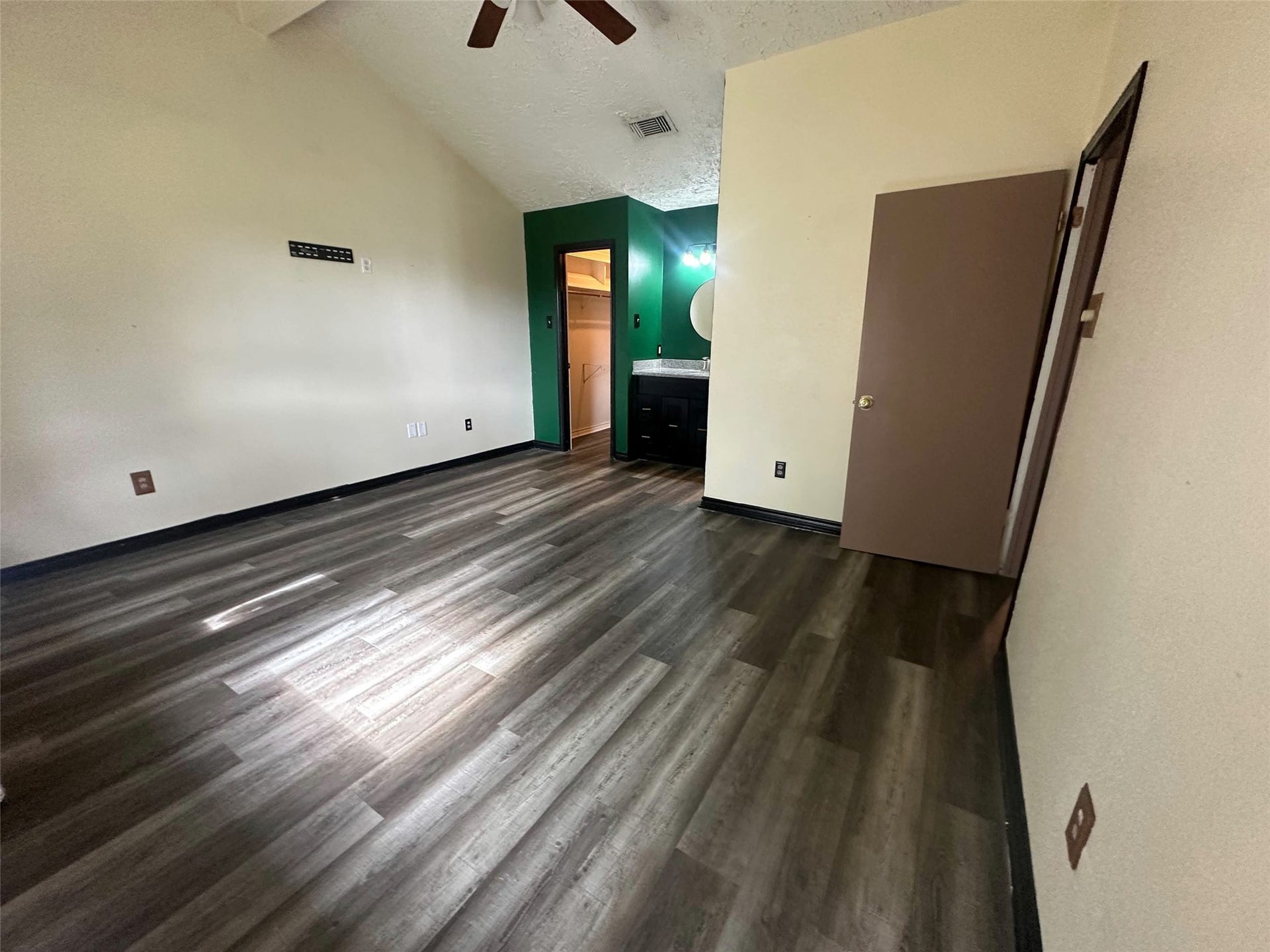 Unfurnished bedroom with plank flooring, attached vanity area and adjacent closet.