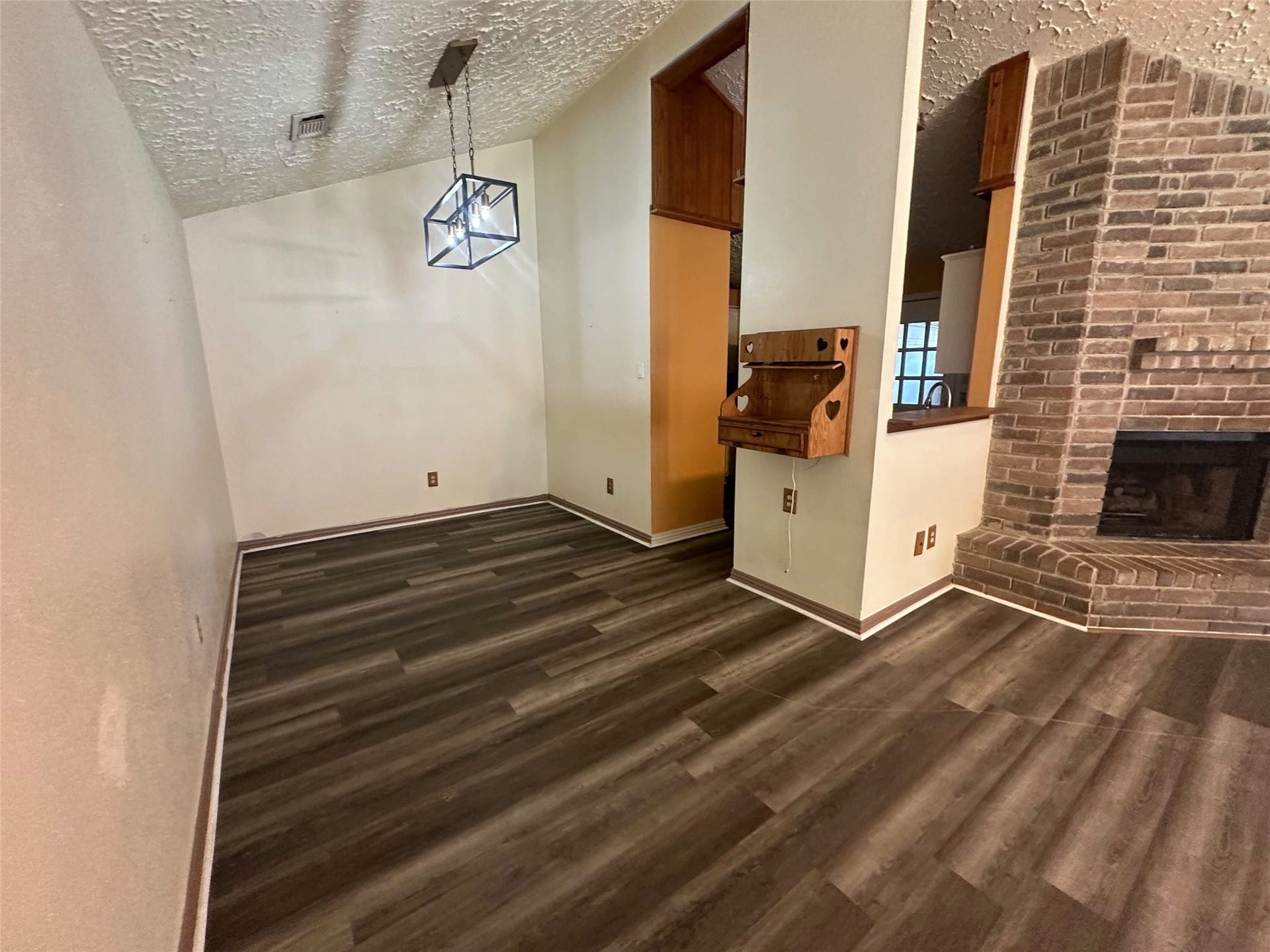Bright open dining area with durable plank flooring, statement pendant, fixed wood hutch and brick-fireplace connection.