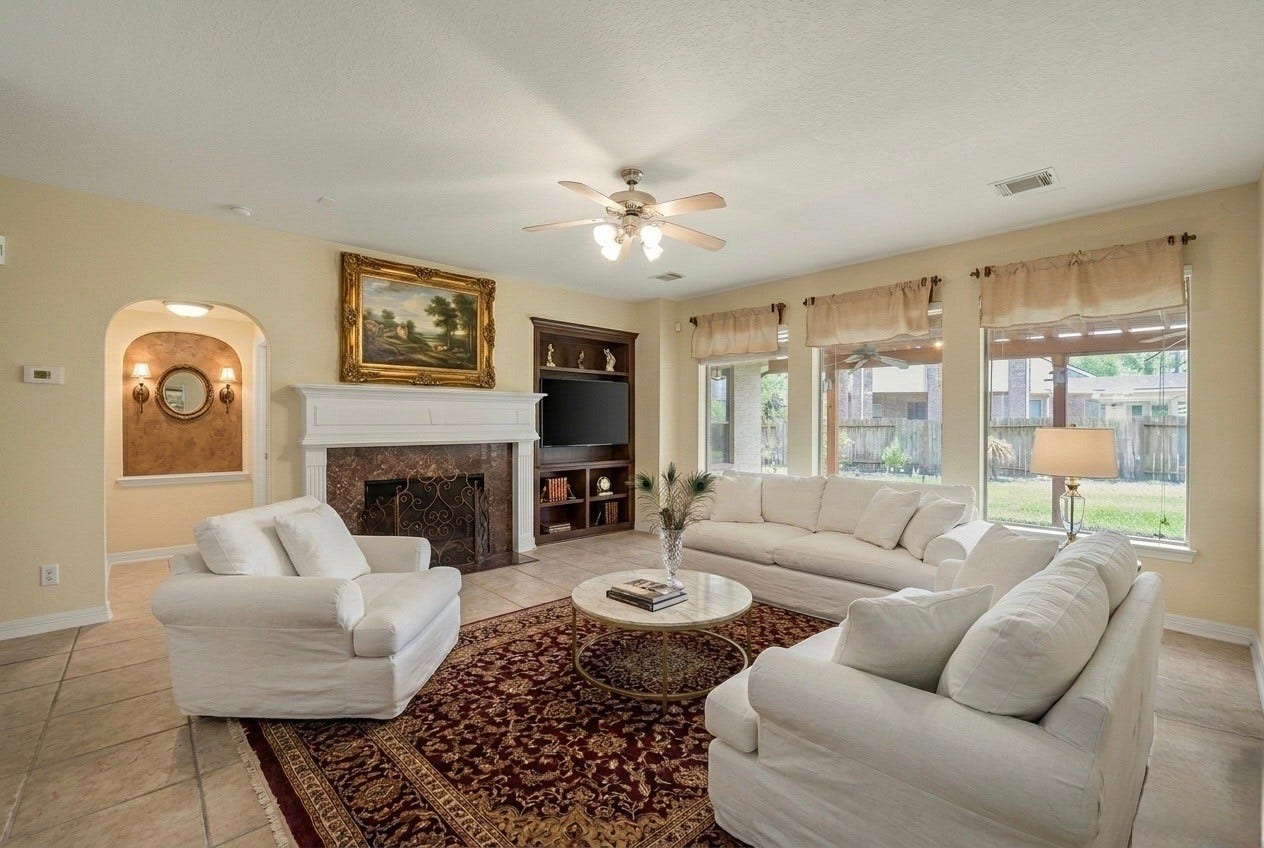 21603 Statfield Glen, Katy, TX 77450 The family room is a warm and inviting space, featuring a gas fireplace with a beautiful wood mantle, elegant finger molding, and built-in shelves. Natural light floods the room through a wall of windows dressed with curtains, while a ceiling fan with a light fixture keeps the space comfortable year-round.