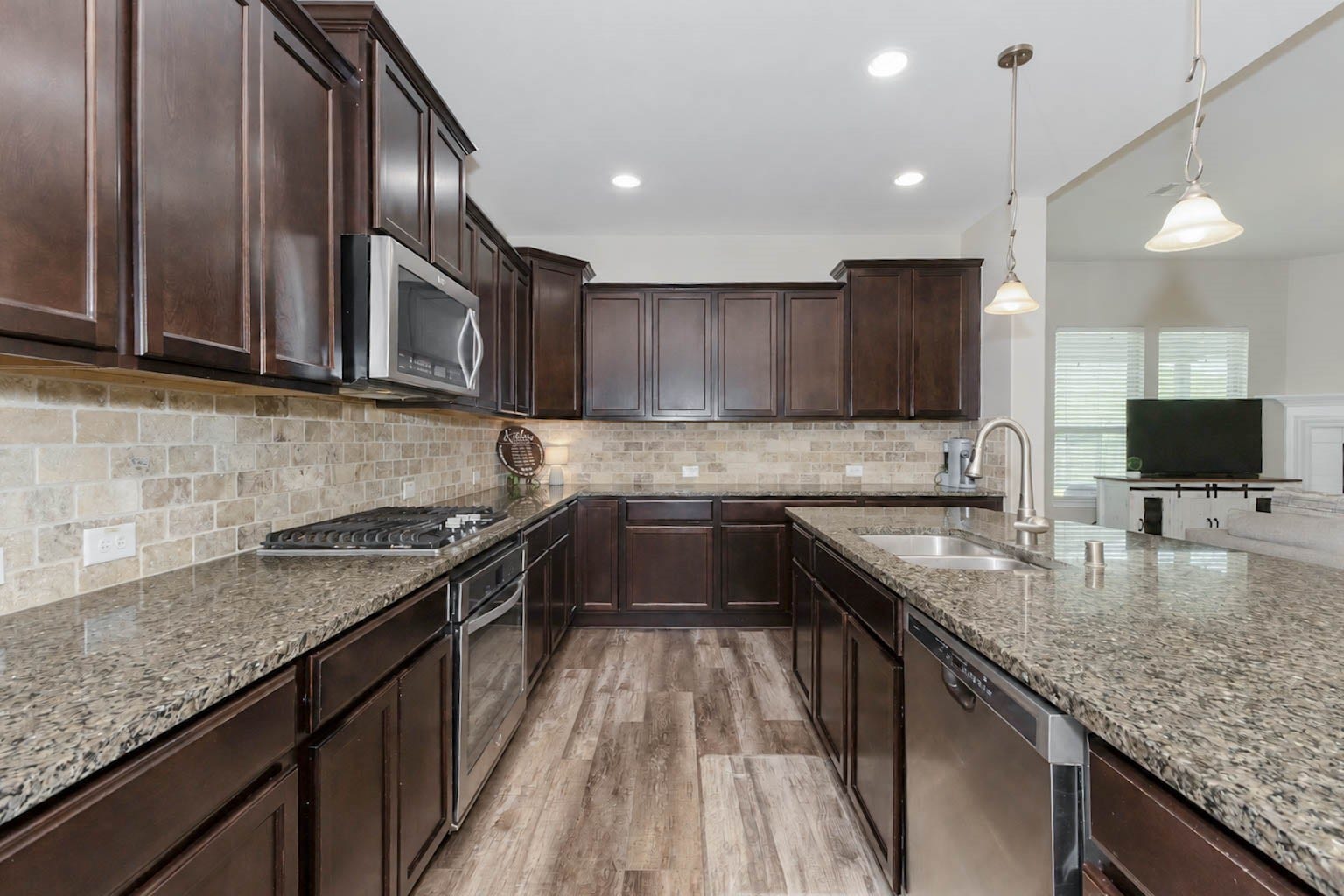 30218 Creekside Drive, Brookshire, TX 77423 Spacious chef's kitchen with rich dark wood cabinetry, granite countertops, and stainless steel appliances, complemented by a warm stone backsplash.