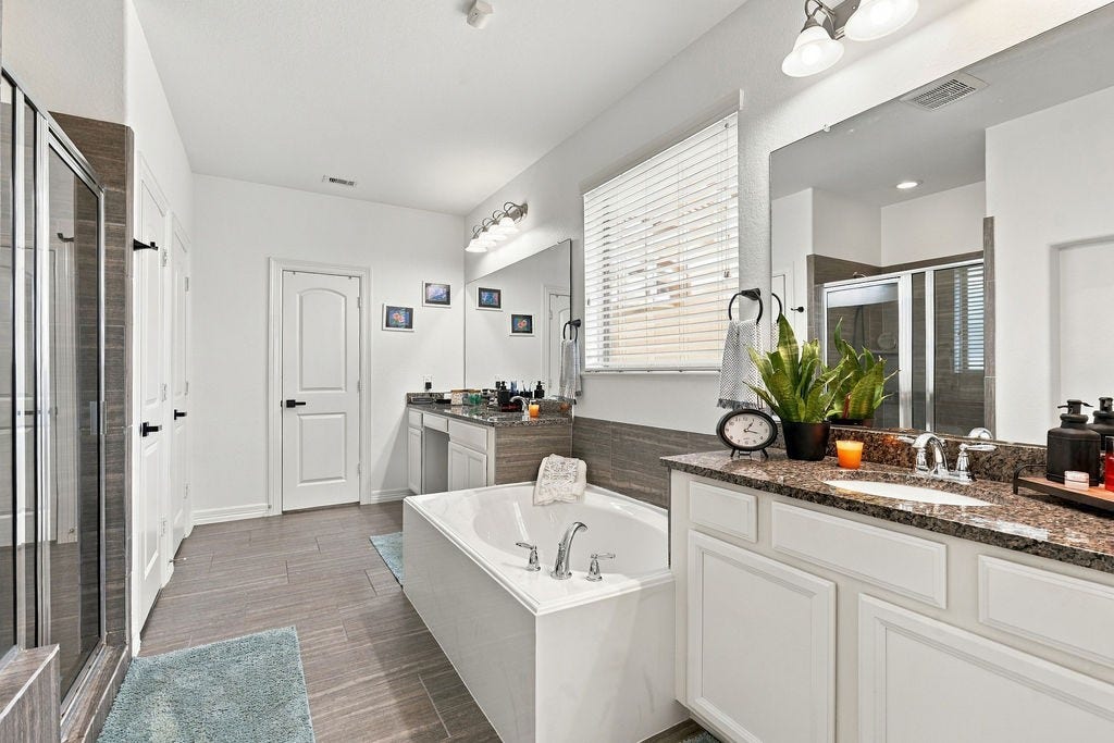 9918 Hubble Drive, Iowa Colony, TX 77583 Elegant bathroom featuring a spacious soaking tub, dual sinks with granite countertops, and a walk-in shower, all accented by modern fixtures and abundant natural light.