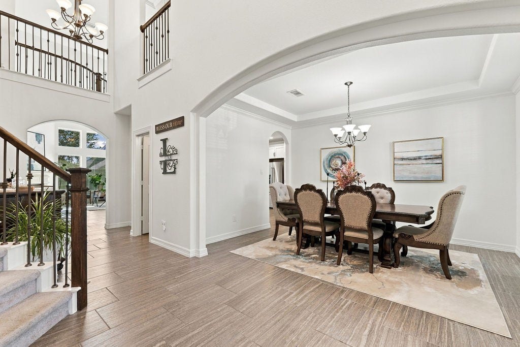 9918 Hubble Drive, Iowa Colony, TX 77583 Elegant dining area with a sophisticated chandelier, beautifully set beneath a coffered ceiling, adjacent to a grand staircase with wrought iron railings.