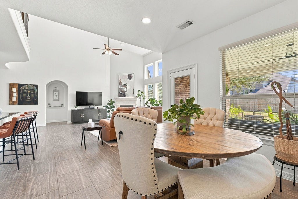 9918 Hubble Drive, Iowa Colony, TX 77583 Spacious and bright open-concept living area with high ceilings, featuring a cozy seating arrangement, elegant breakfast space, and modern kitchen bar, all beautifully lit by large windows.