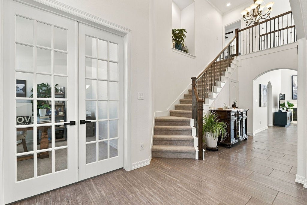 9918 Hubble Drive, Iowa Colony, TX 77583 Elegant entryway featuring a grand staircase, stylish French doors leading to a cozy office, and modern tile flooring, all under a sophisticated chandelier.