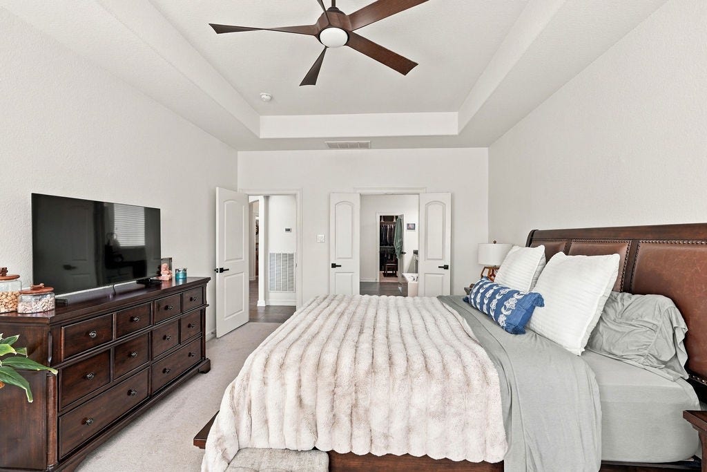 9918 Hubble Drive, Iowa Colony, TX 77583 Spacious primary bedroom featuring a cozy bed, elegant dark wood furniture, and a modern ceiling fan, all complemented by soft, neutral walls for a tranquil retreat.