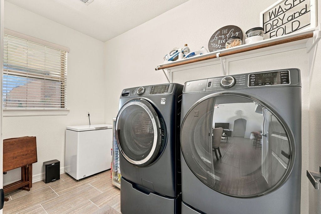 9918 Hubble Drive, Iowa Colony, TX 77583 Spacious laundry room featuring modern washer and dryer, ample shelving for storage, and natural light from a large window.