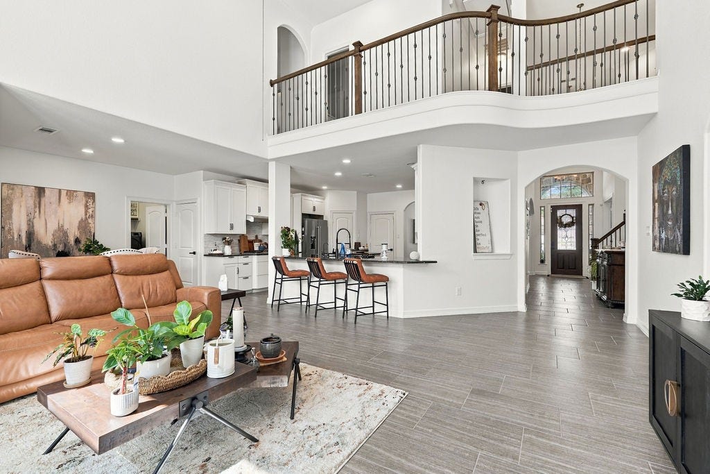 9918 Hubble Drive, Iowa Colony, TX 77583 Spacious open-concept living area with high ceilings, featuring a modern kitchen with a breakfast bar, elegant wood-look flooring, and a grand staircase with a stylish railing.