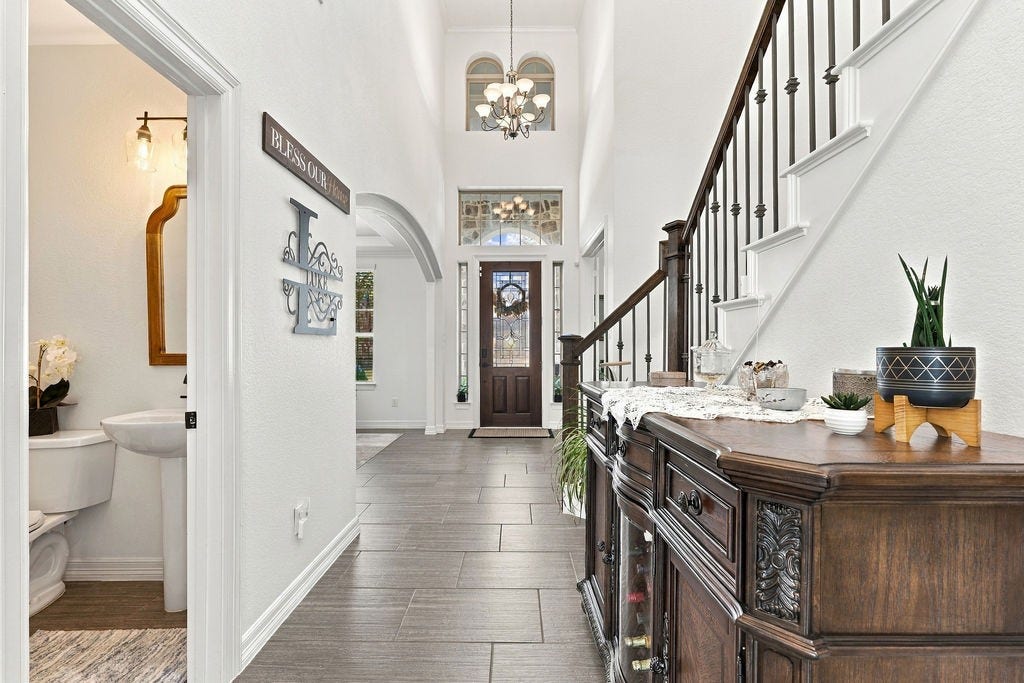9918 Hubble Drive, Iowa Colony, TX 77583 Elegant entryway with a grand staircase, high ceilings, and a welcoming chandelier. The space leads to a bright interior, creating a warm first impression.