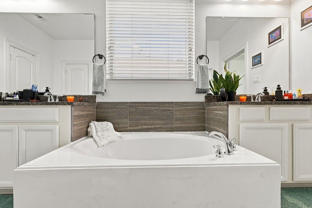 9918 Hubble Drive, Iowa Colony, TX 77583 Luxurious bathroom featuring a spacious soaking tub, dual vanities with elegant granite countertops, and modern finishes, creating a serene retreat.