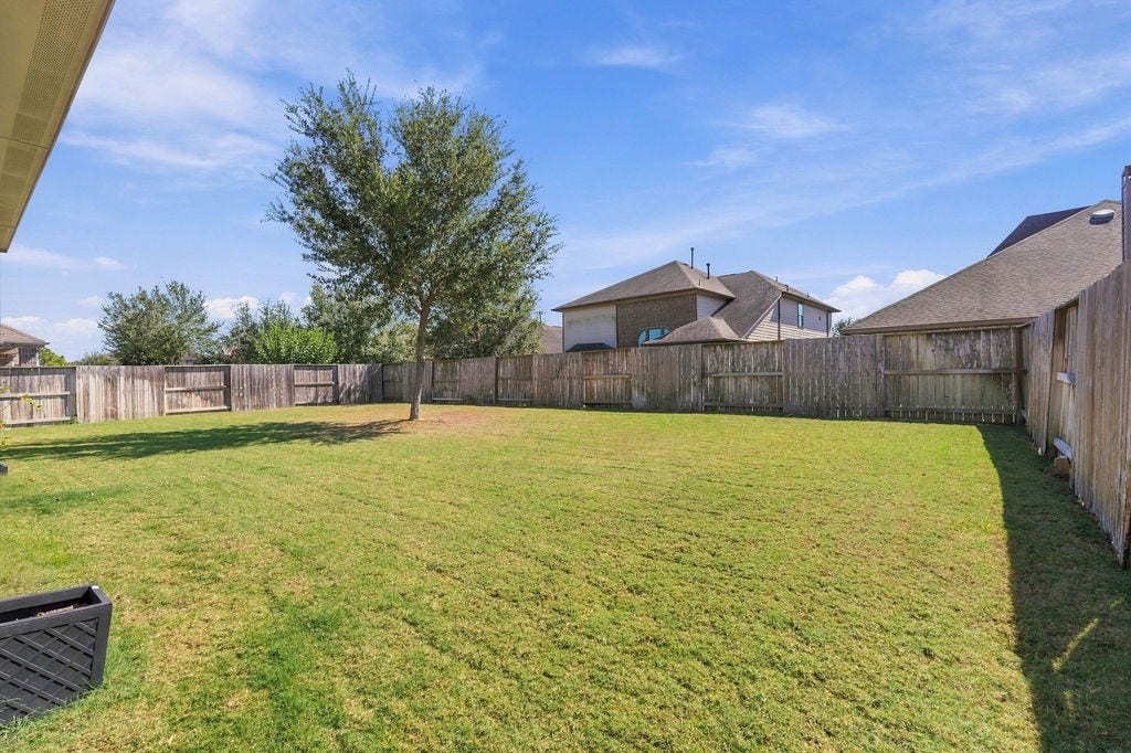 9918 Hubble Drive, Iowa Colony, TX 77583 Expansive fenced backyard with lush green lawn and a single mature tree, perfect for outdoor activities and relaxation.