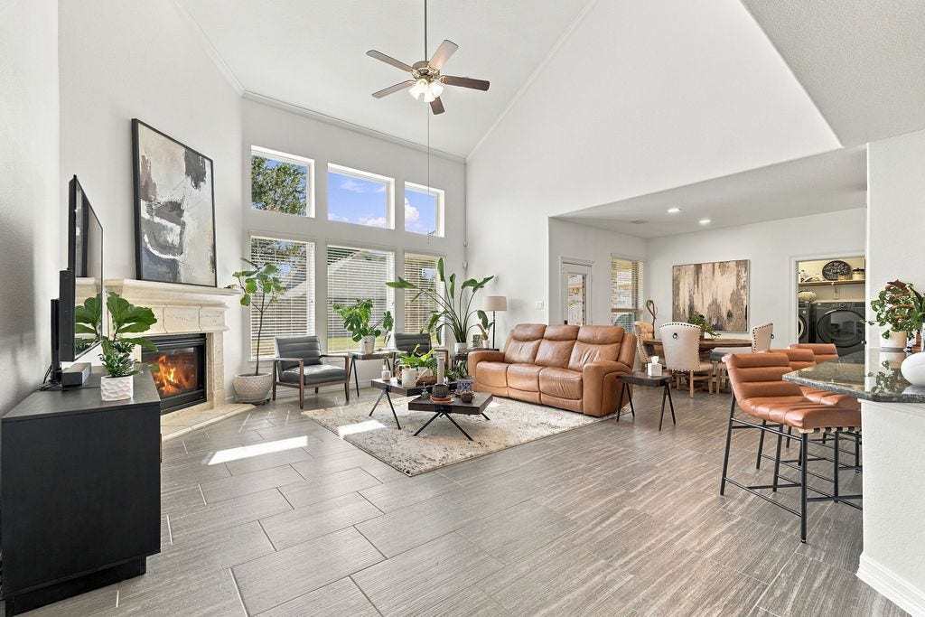 9918 Hubble Drive, Iowa Colony, TX 77583 Spacious living area with high ceilings, abundant natural light from large windows, and a cozy fireplace. The open layout connects seamlessly to the dining and kitchen areas, offering a perfect setting for entertaining or relaxing.