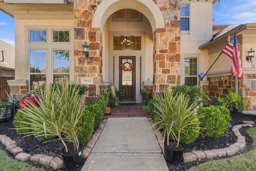 9918 Hubble Drive, Iowa Colony, TX 77583 Charming stone-accented entryway with lush landscaping, welcoming front door, and elegant archway, creating a warm and inviting first impression.