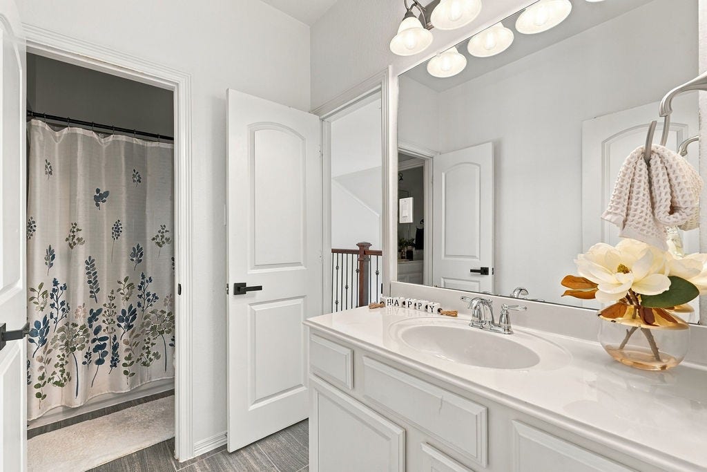 9918 Hubble Drive, Iowa Colony, TX 77583 Bright and inviting bathroom featuring a spacious vanity with a large mirror, elegant light fixtures, and a charming floral shower curtain.
