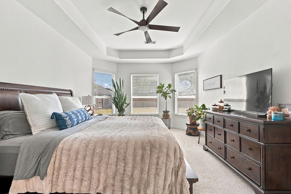 9918 Hubble Drive, Iowa Colony, TX 77583 Spacious master bedroom with a cozy atmosphere, featuring a plush bed, large windows for ample natural light, and elegant ceiling fan.