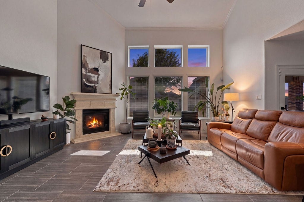 9918 Hubble Drive, Iowa Colony, TX 77583 Spacious living room with high ceilings and large windows showcasing a stunning sunset view. Features a cozy fireplace, elegant tile flooring, and ample space for large furniture.