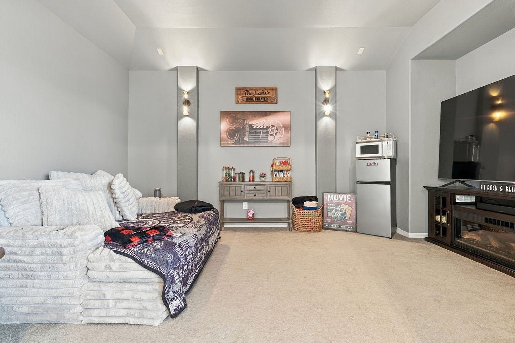 9918 Hubble Drive, Iowa Colony, TX 77583 Cozy entertainment room featuring plush seating, a large flat-screen TV, and a mini refreshment area with a microwave and fridge, perfect for movie nights.