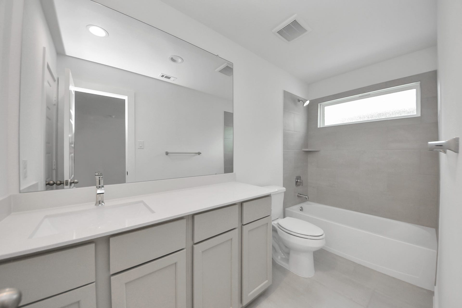 Secondary bath features tile flooring, bath/shower combo with tile surround, light stained wood cabinets, beautiful light countertop.