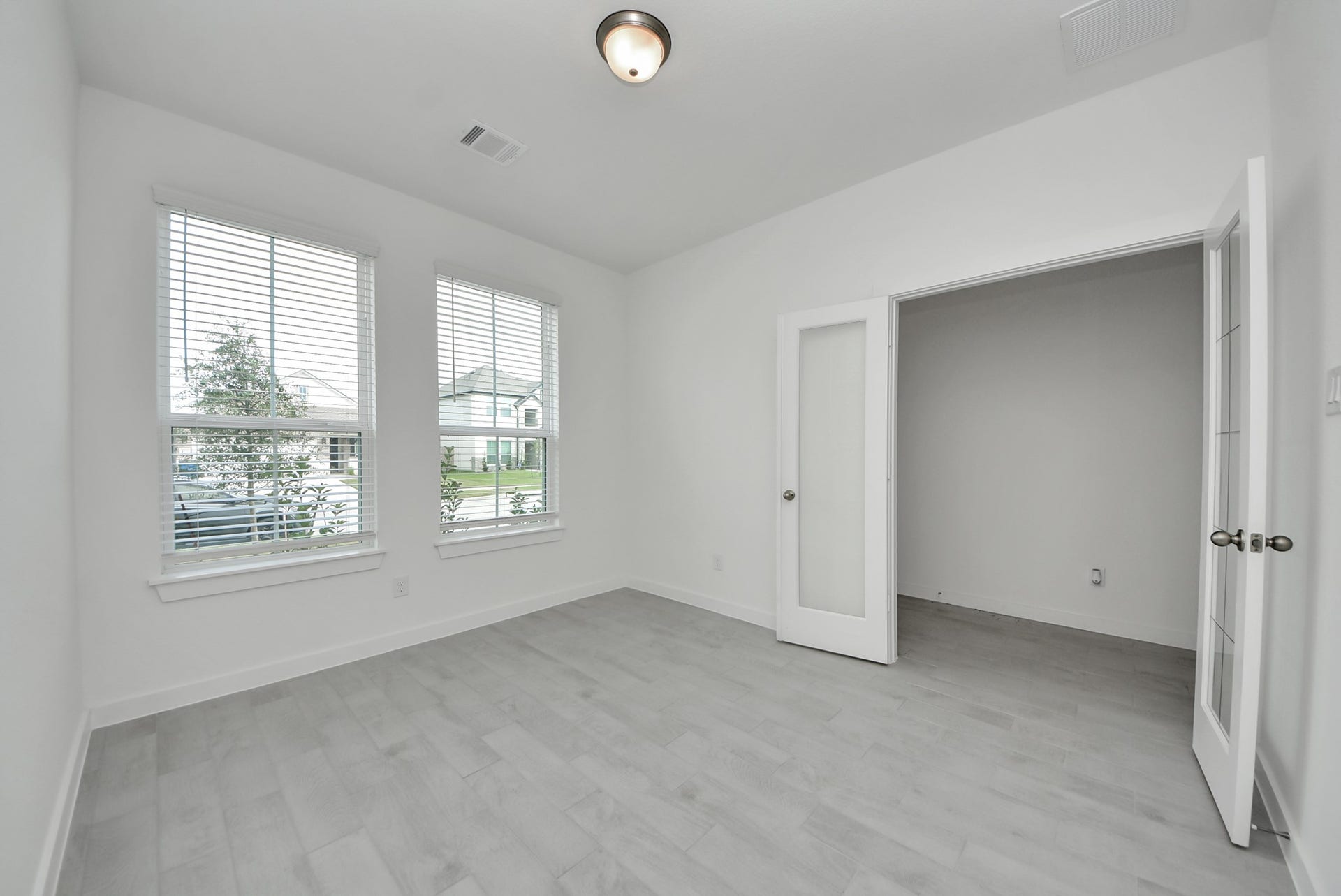 Experience the perfect blend of sophistication and warmth in this home office, boasting elegant wood-look tile flooring and flooded with natural light from expansive windows and French doors.