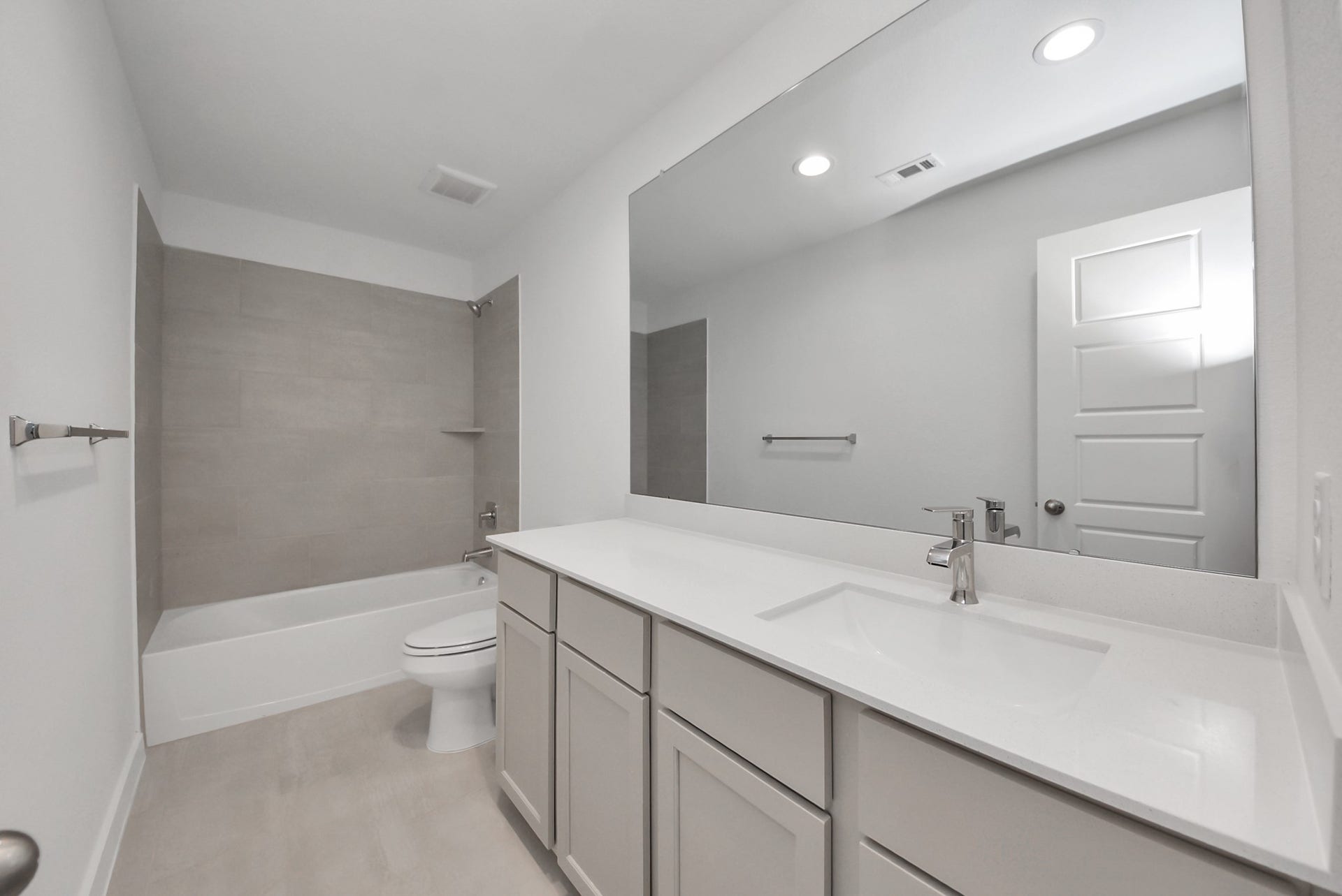 Secondary bath features tile flooring, bath/shower combo with tile surround, light stained wood cabinets, beautiful light countertop.