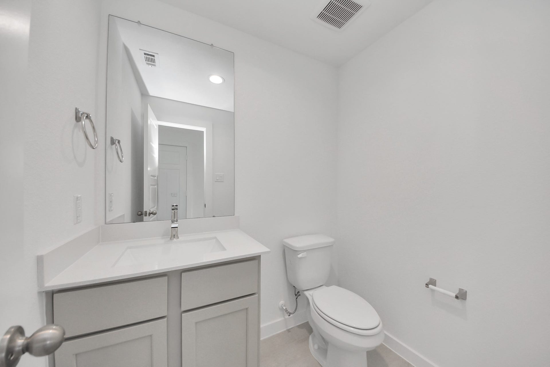 Sophisticated half bathroom adorned with contemporary finishes. The elegant 5-panel door welcomes you to a space where style meets functionality. Notice the sleek hardware accents that add a touch of modern charm. The vanity boasts light-colored countertops, beautifully complemented by a tasteful vanity light, creating a well-lit and inviting atmosphere.
