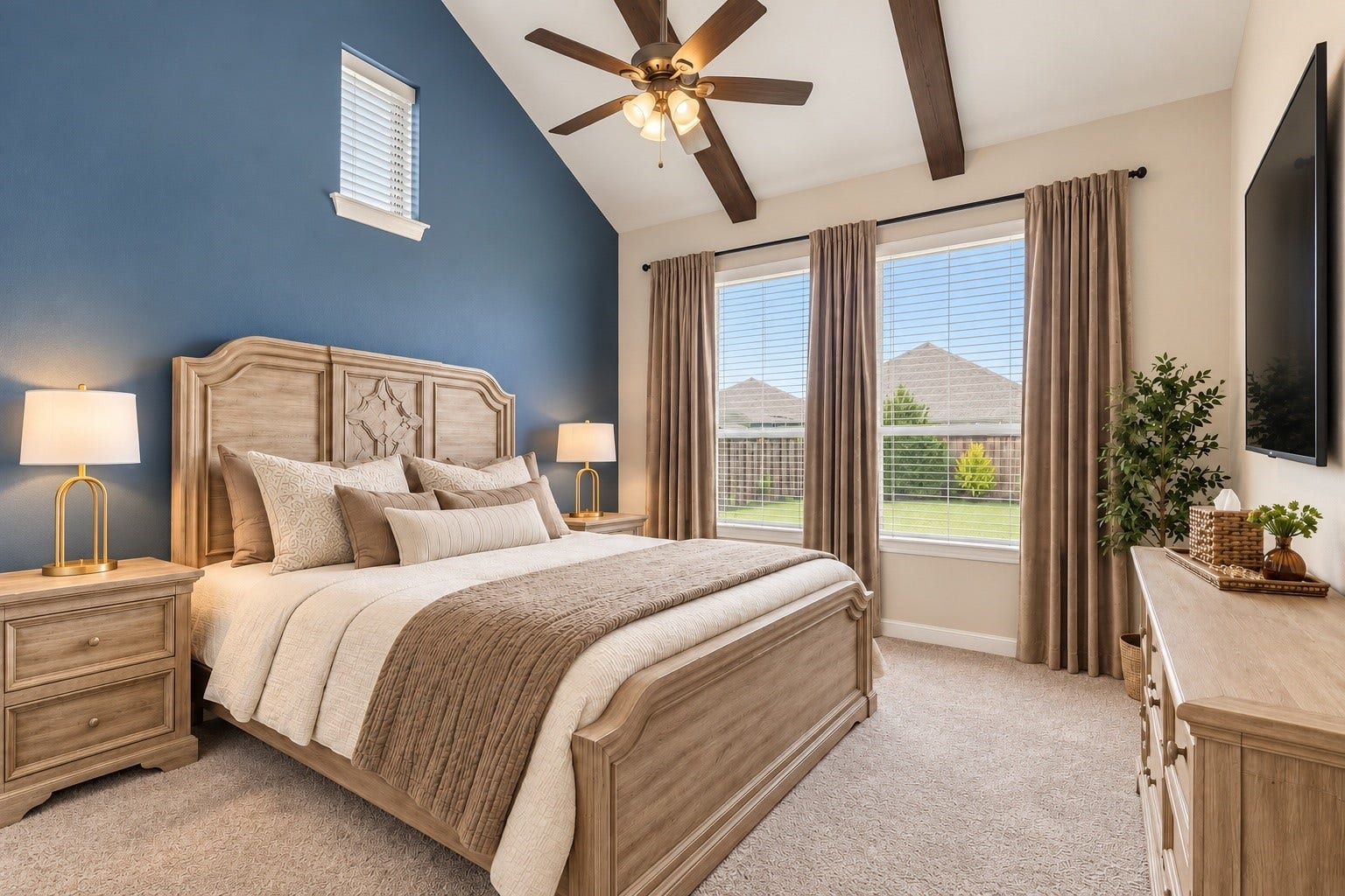 Spacious first-floor primary retreat featuring a vaulted ceiling with exposed decorative beams, ceiling fan, plush carpeting, and large windows overlooking the backyard.