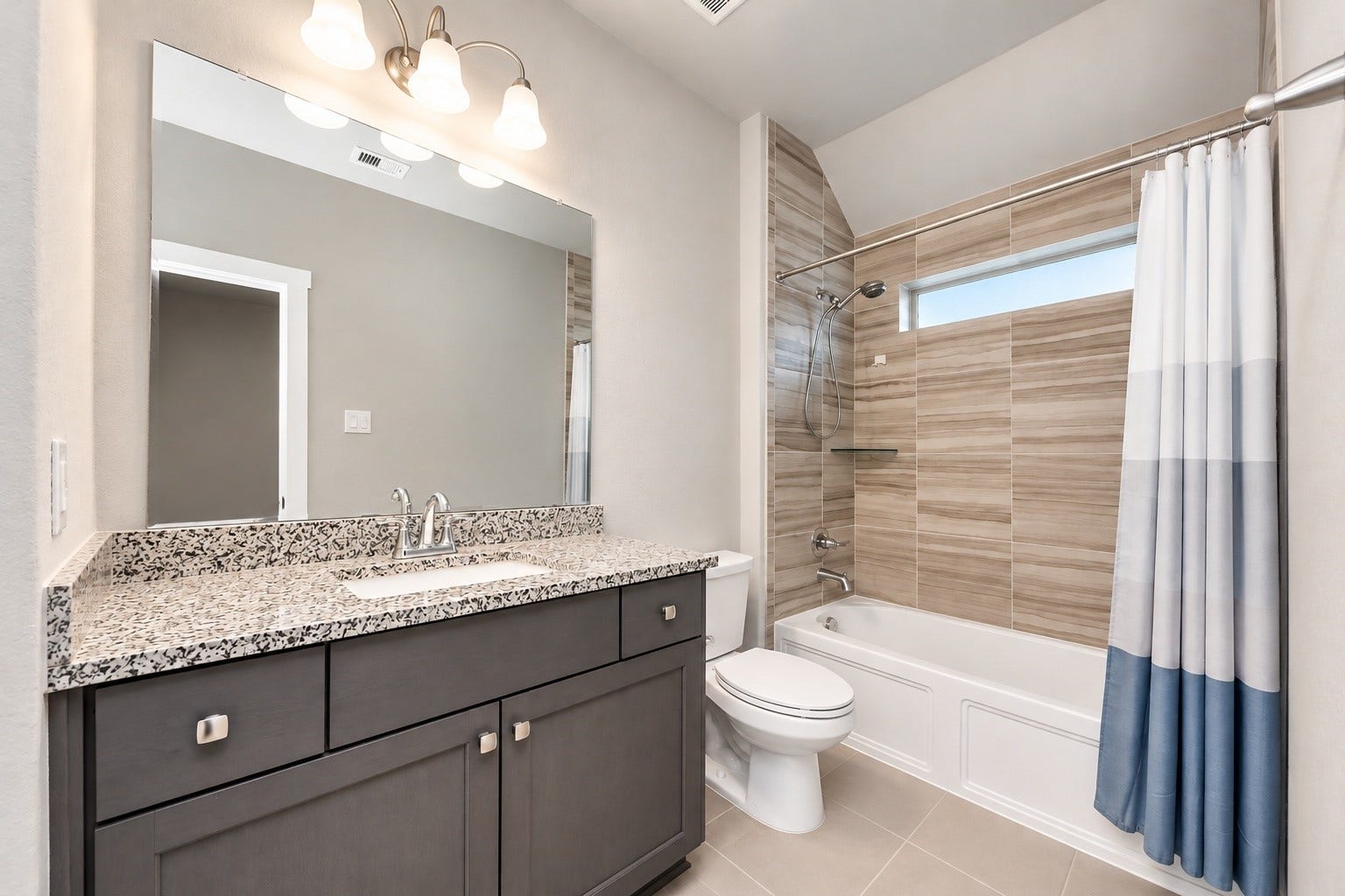 Spacious secondary bathroom featuring dual vanities, a large mirror, ample cabinetry, and a tiled tub/shower combination.