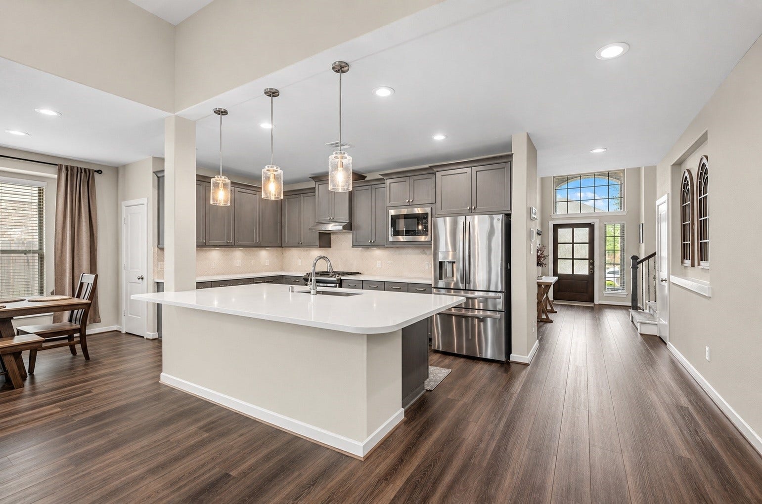 Spacious open-concept kitchen featuring a large center island with breakfast bar seating, quartz/granite countertops, pendant lighting, and abundant cabinetry.