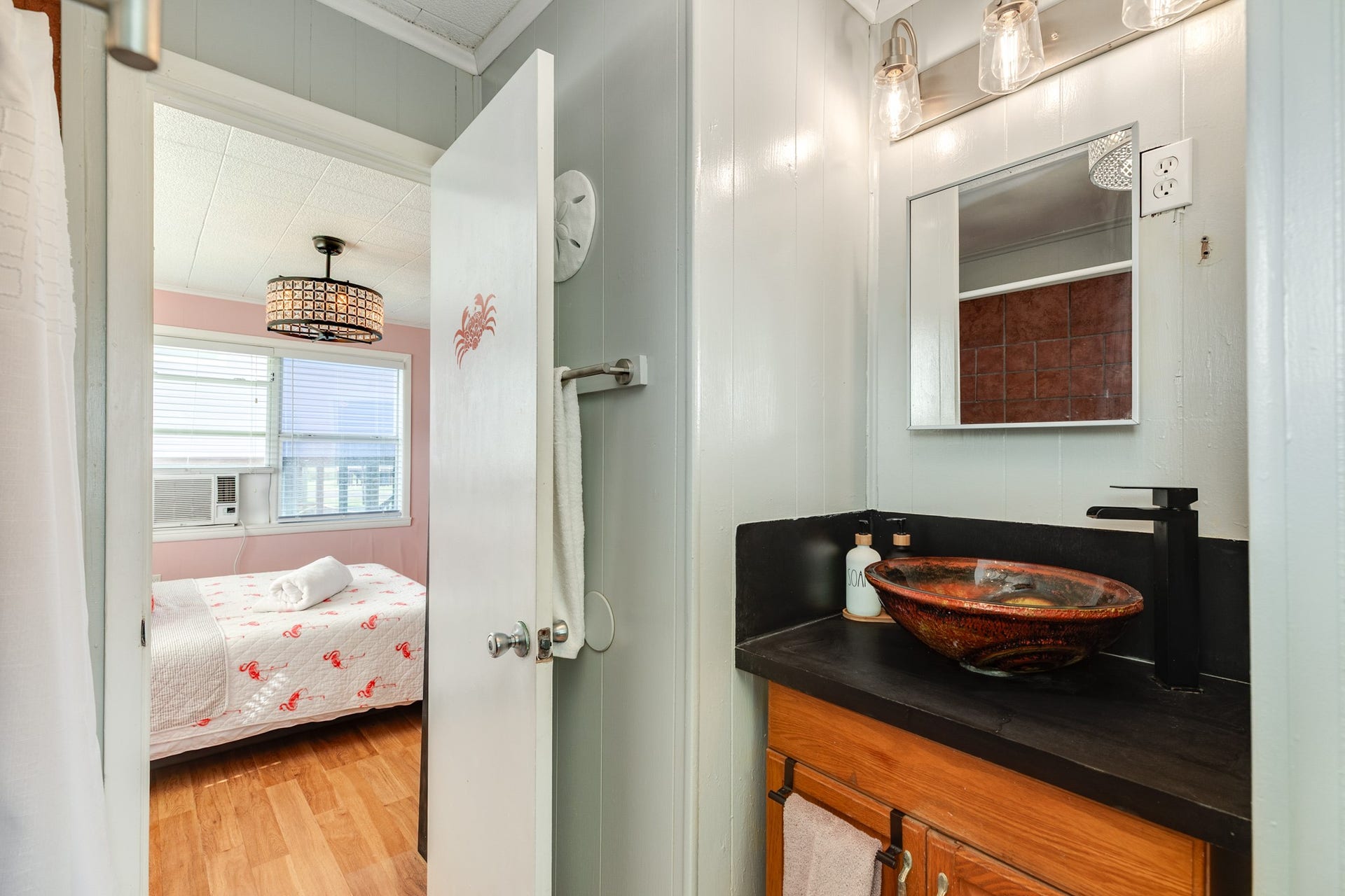 Compact bathroom features a distinctive vessel sink, dark countertop, wood vanity, and contemporary black faucet beneath a wall mirror.