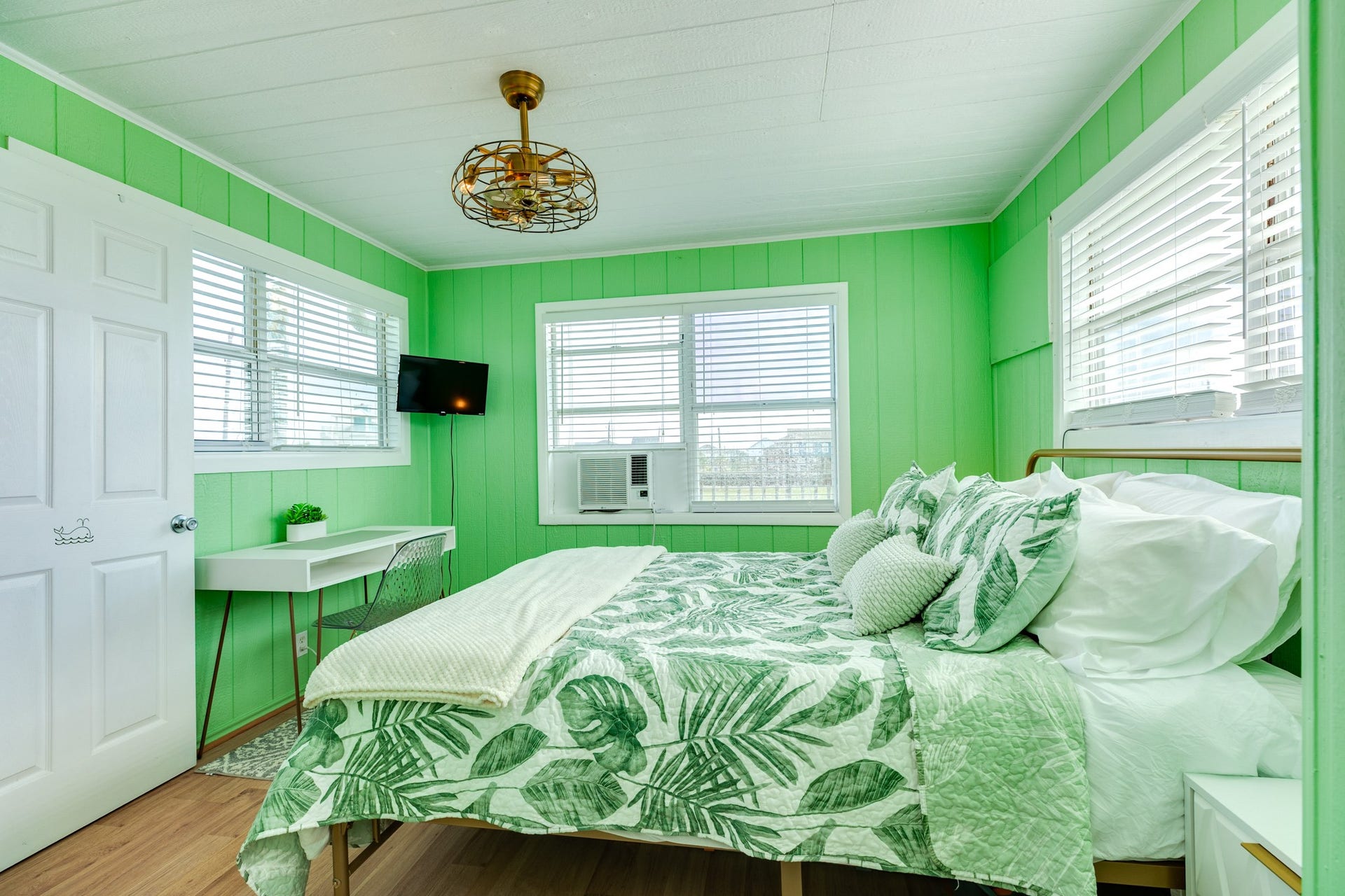 Multiple windows bring natural light into this colorful bedroom, which also includes a wall-mounted TV and window air-conditioning unit.