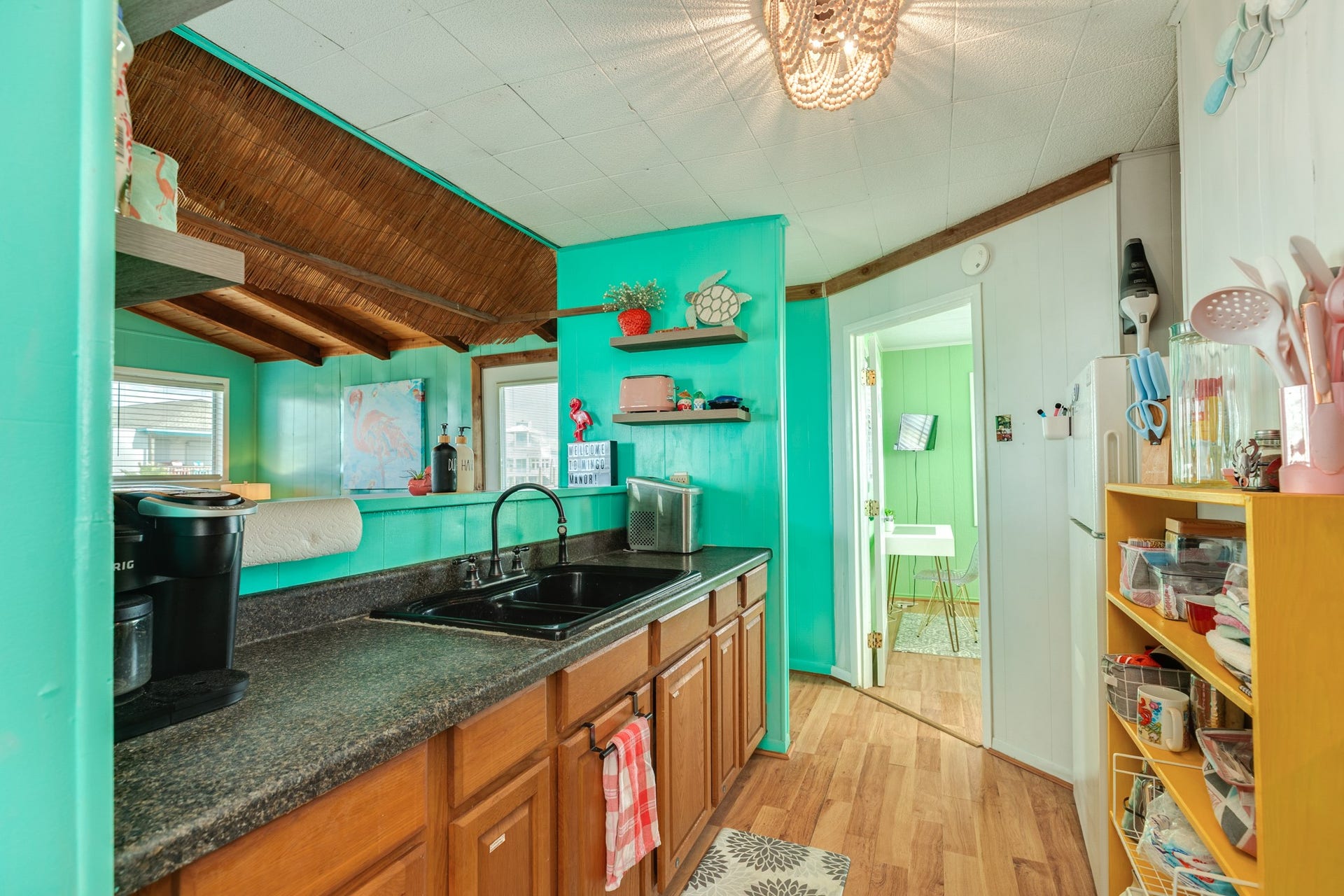 Another kitchen view highlights the long countertop, double-basin sink, storage cabinetry, and pass-through connection to the living room.