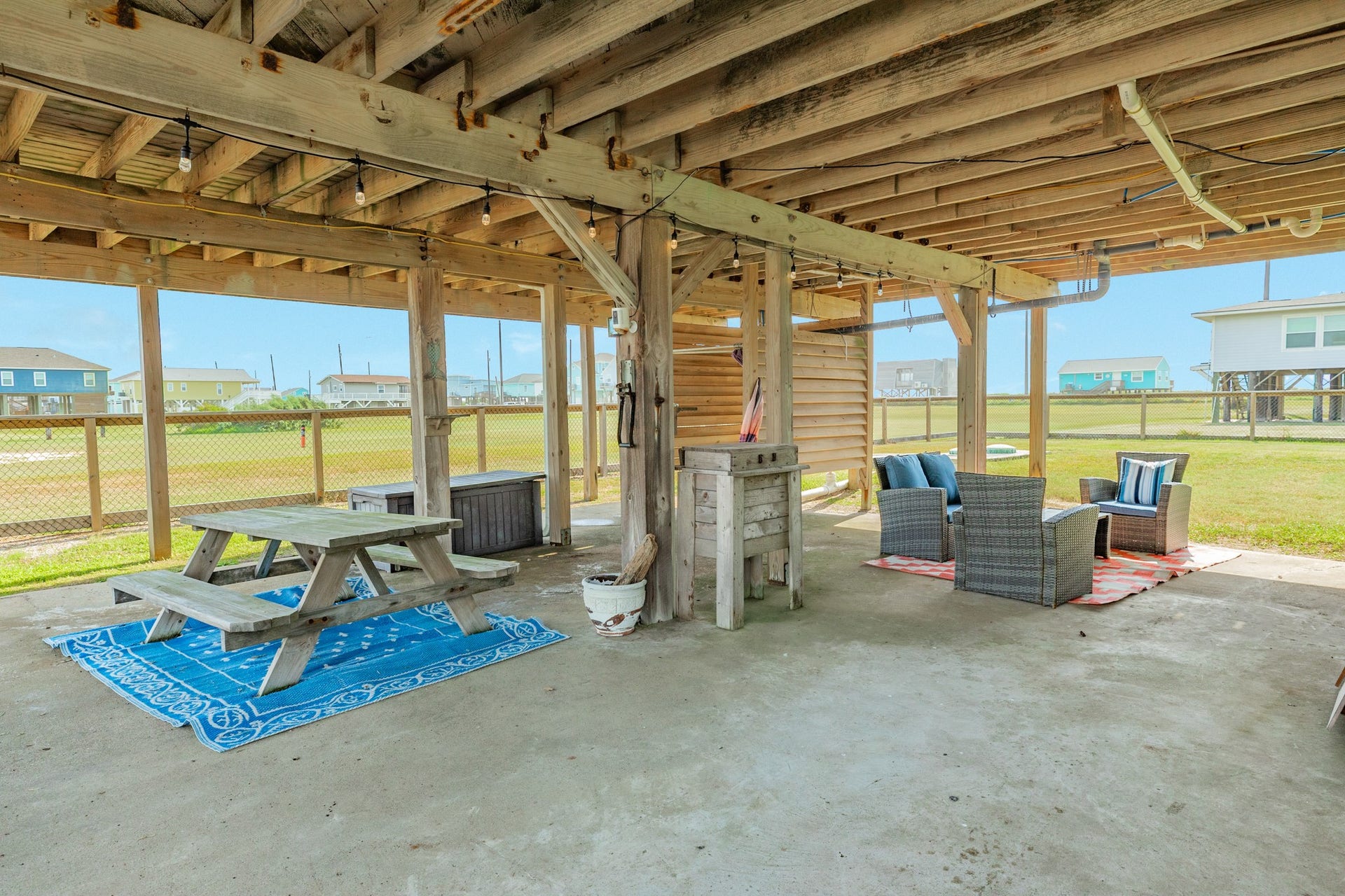 Expansive covered area beneath the home offers ample room for outdoor dining and lounging, with string lighting and a concrete surface for easy upkeep.