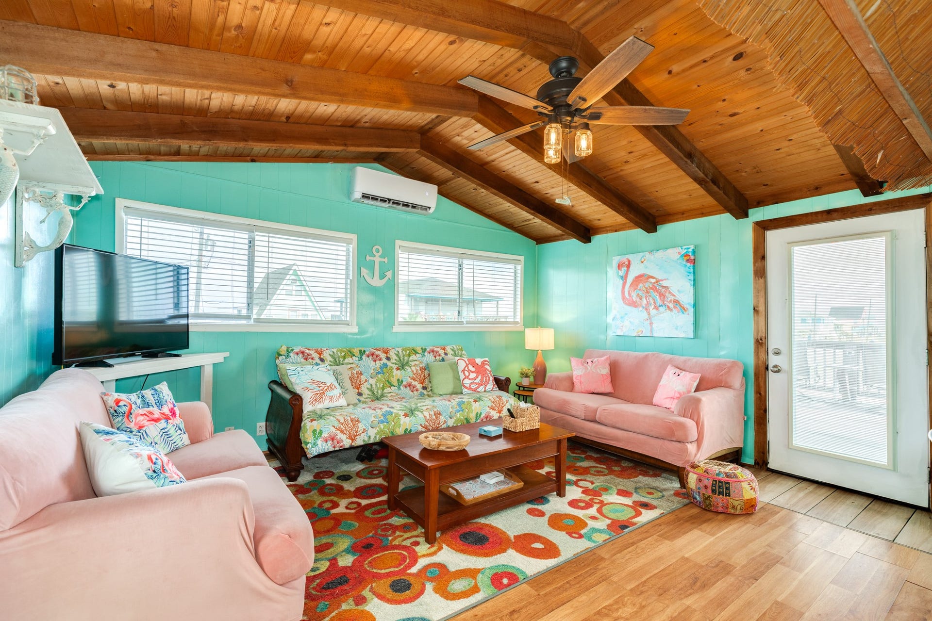 Bright living area features colorful coastal dcor, abundant windows, wood-look flooring, and a warm vaulted wood ceiling with exposed beams.
