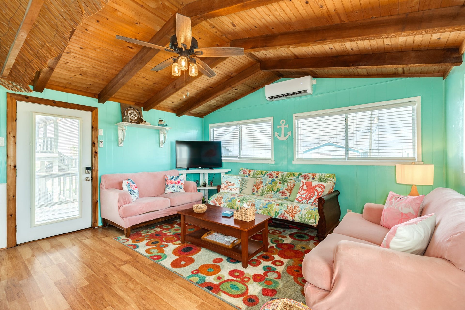 Bright coastal-inspired living room features a vaulted wood-plank ceiling with exposed beams, abundant windows, wood-look flooring, and a mini-split system.