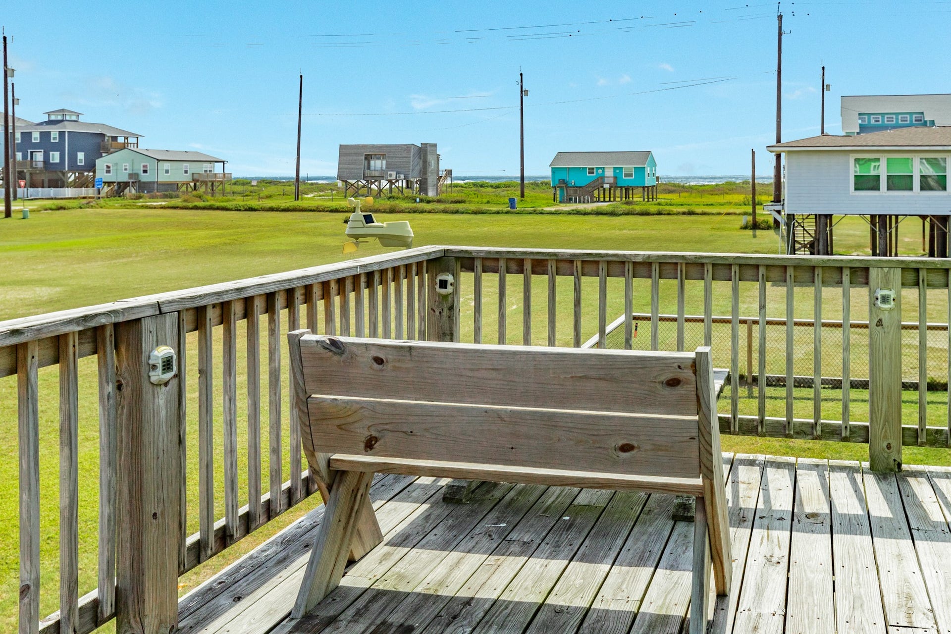Deck seating overlooks the large grassy area with a glimpse of the Gulf visible beyond the neighboring homes.