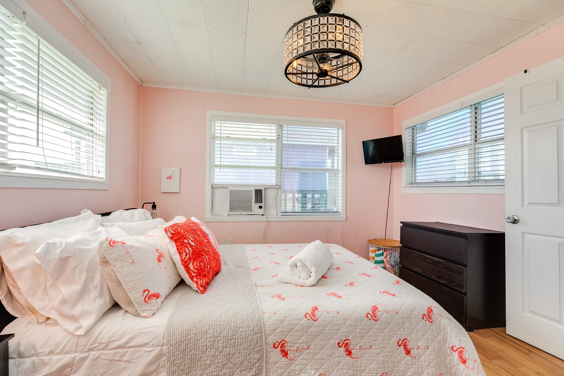 Additional view of the pink bedroom highlights windows on three sides, wood-look flooring, a wall-mounted TV, and a window air-conditioning unit.