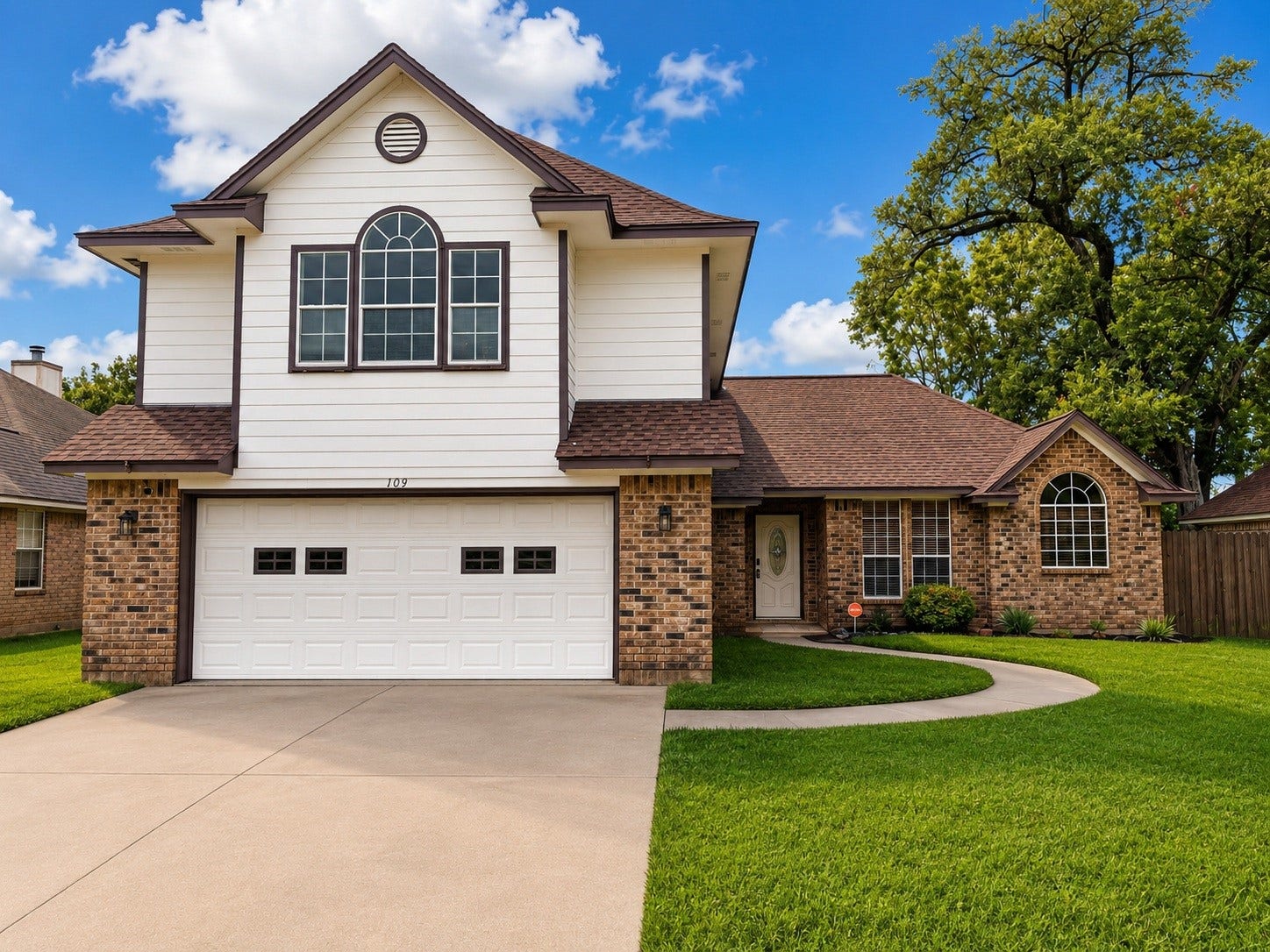 This charming two-story home features a mix of brick and siding, a spacious two-car garage, and a well-maintained front lawn with mature trees. It offers a welcoming curb appeal with a curved walkway leading to the front door.