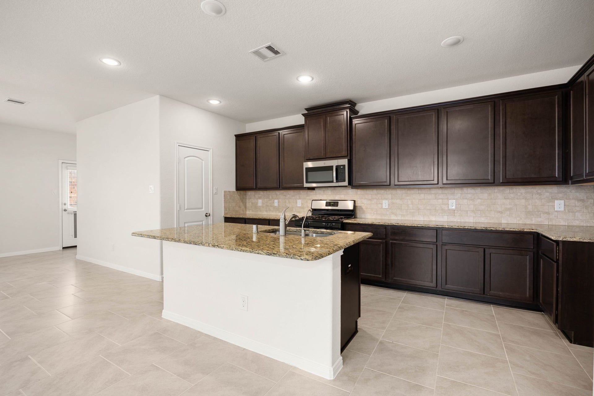 23643 Balzano Court, Katy, TX 77493 A chef-inspired kitchen designed for gathering, featuring rich cabinetry, granite countertops, stainless steel appliances, a spacious pantry, and an oversized island with bar seating. The open-concept layout flows effortlessly into the living and dining areas, making entertaining and everyday living both stylish and functional.