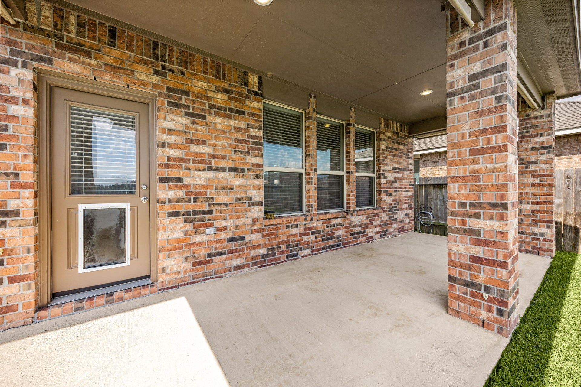 23643 Balzano Court, Katy, TX 77493 Inviting covered back porch highlighting a full brick accent wall, a triple window bank, and a modern exterior door equipped with a built-in pet door.