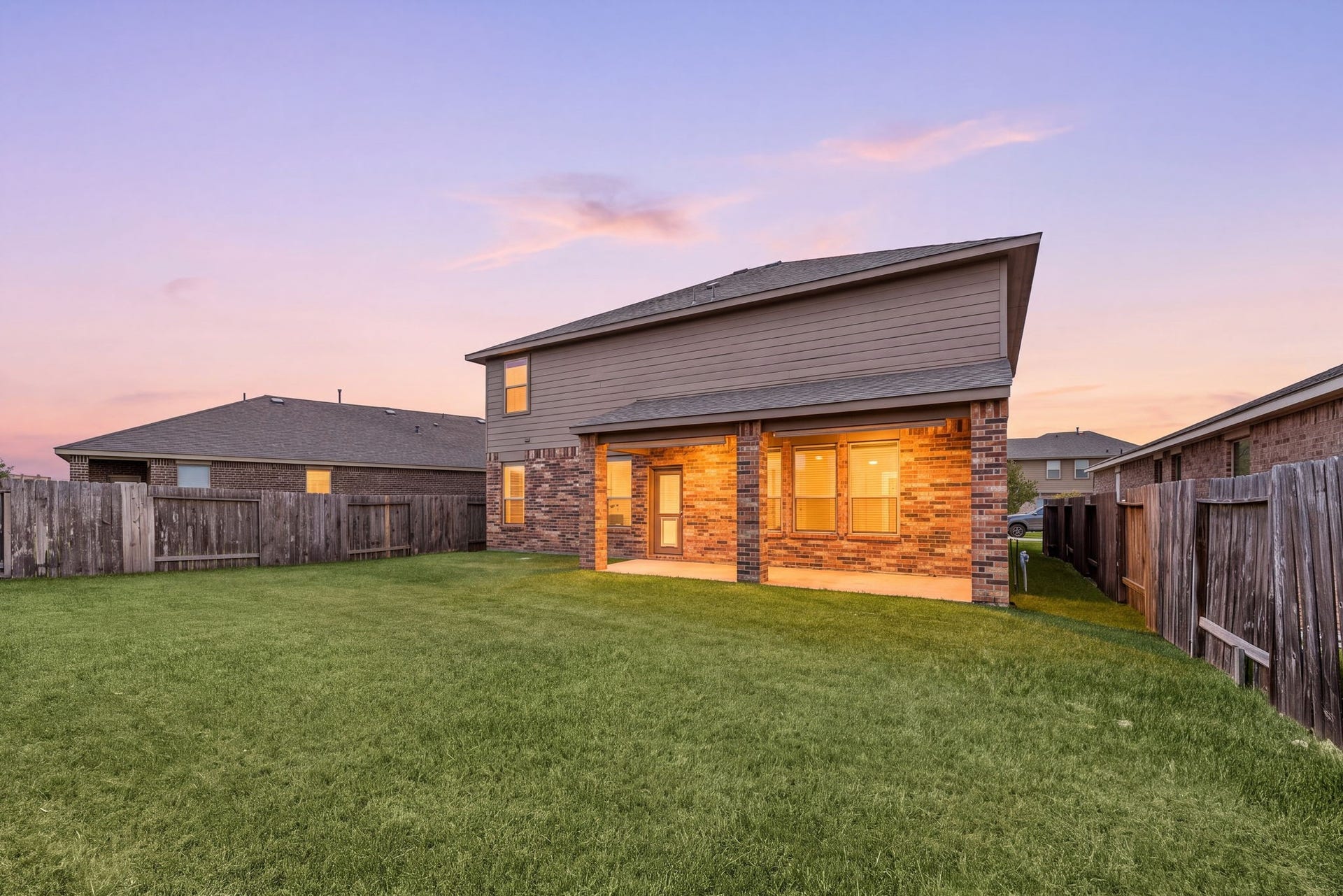 23643 Balzano Court, Katy, TX 77493 Stunning twilight view of the two-story rear exterior highlighting a warm, glowingly lit covered patio and an expansive grassy backyard.